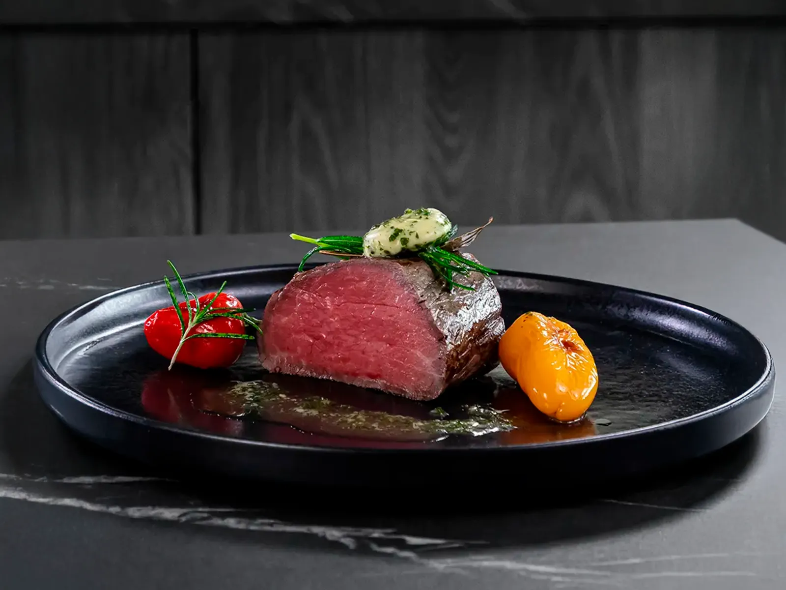 Perfekt gegartes Roastbeef und Ofengemüse auf schwarzem Teller, garniert mit Kräutern.