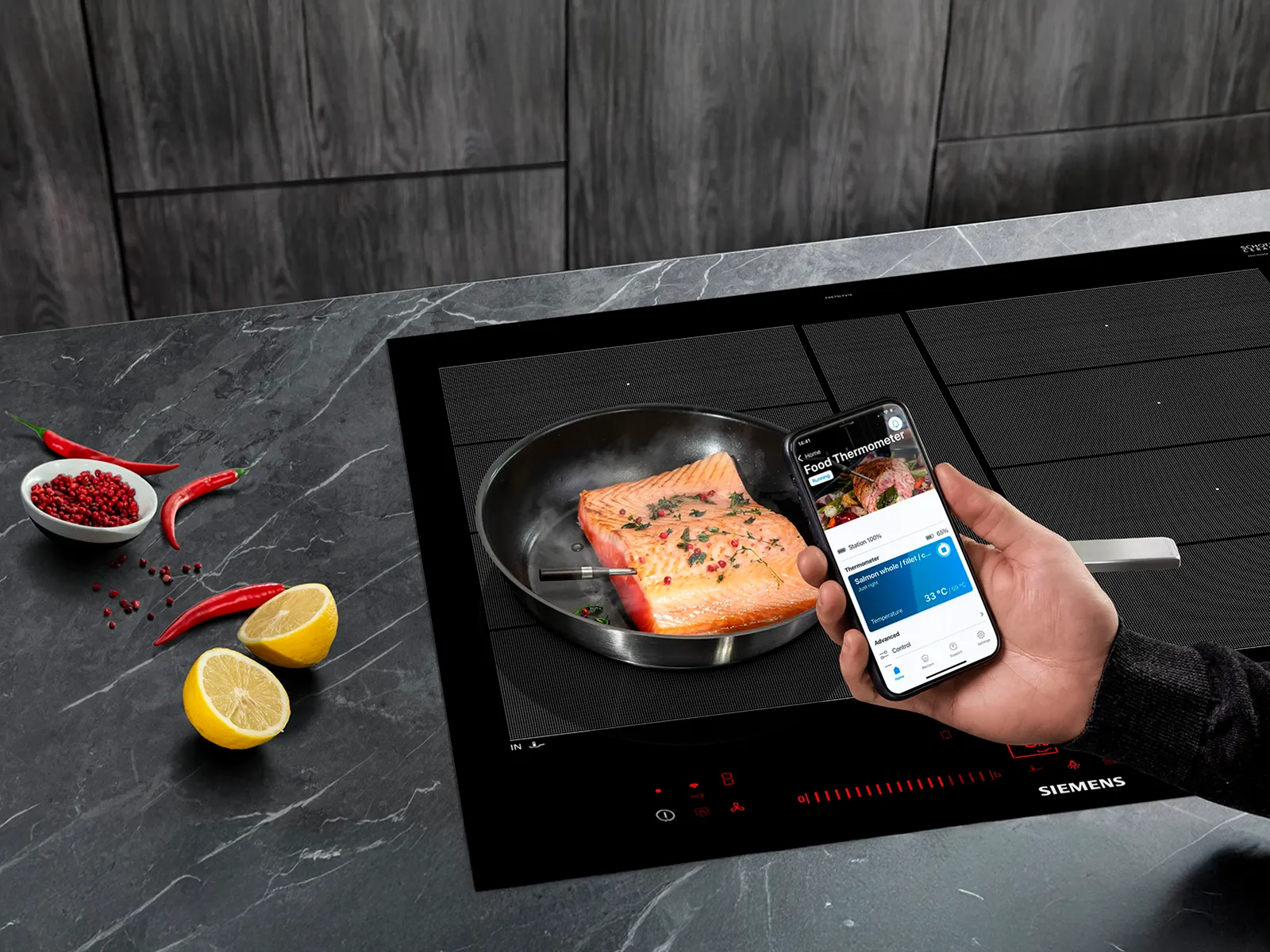 Hand hält ein Smartphone vor Lachs in der Pfanne, der roastingSensor ist eingesetzt.