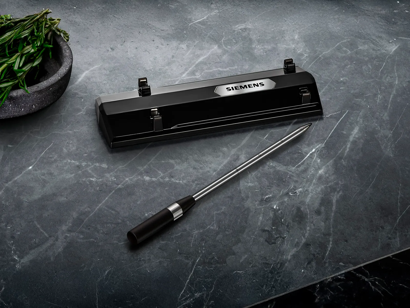 Ein Siemens wireless roastingSensor und seine Ladestation auf einer grauen Marmorarbeitsplatte.