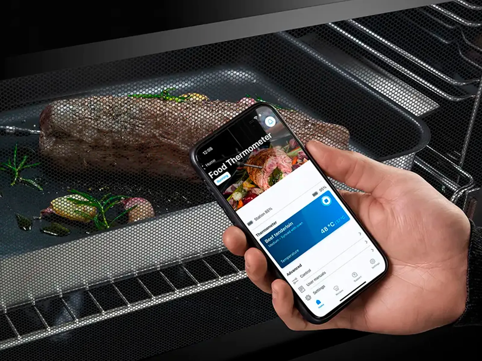 Hand hält Smartphone mit angezeigter Fleischtemperatur vor dem Ofen mit Braten.