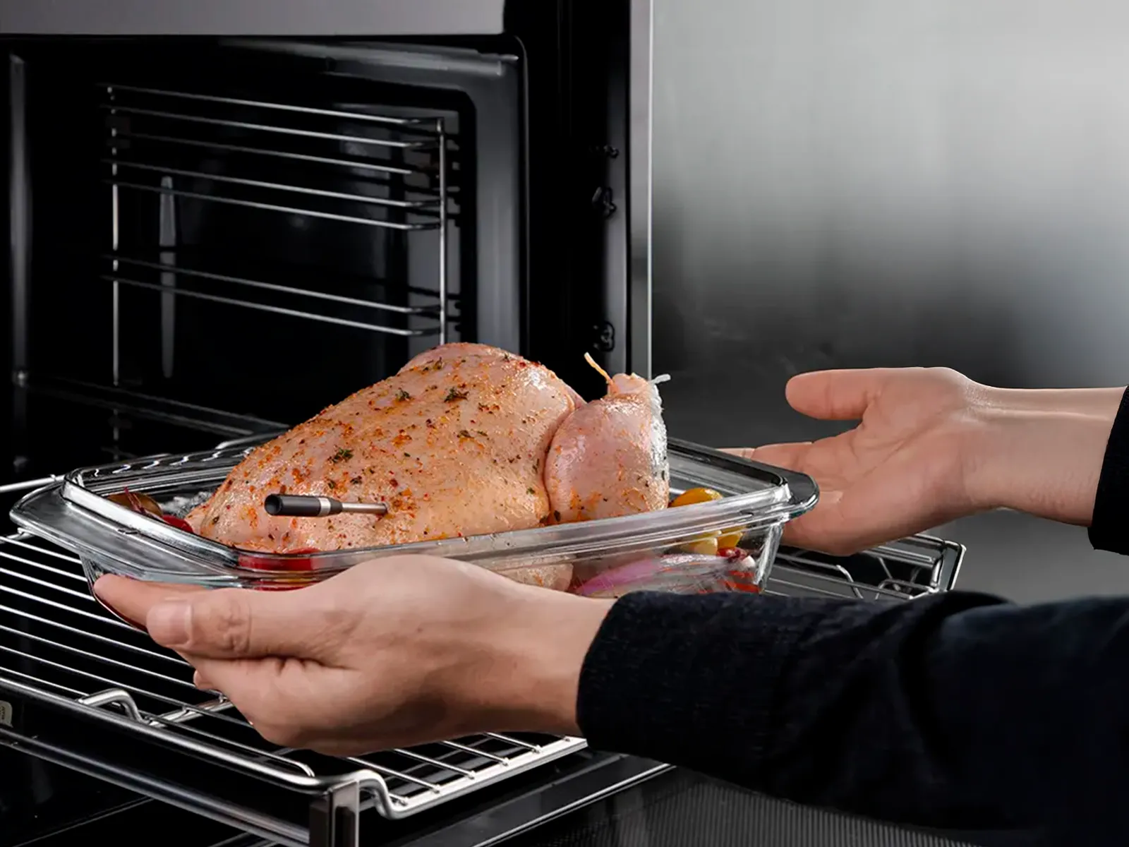 Zwei Hände schieben ein rohes Hähnchen in den Ofen, während der kabellose roastingSensor eingesetzt ist.