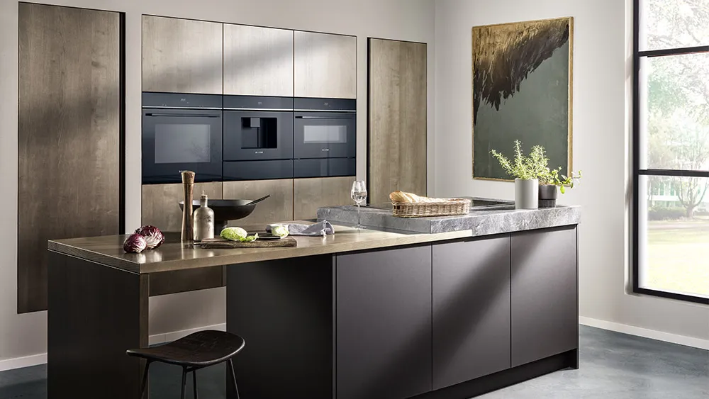 Cucina moderna con mobili scuri, isola sul piano di lavoro in marmo, elettrodomestici da incasso, una grande finestra e arredamento minimalista con piante e opere d'arte.