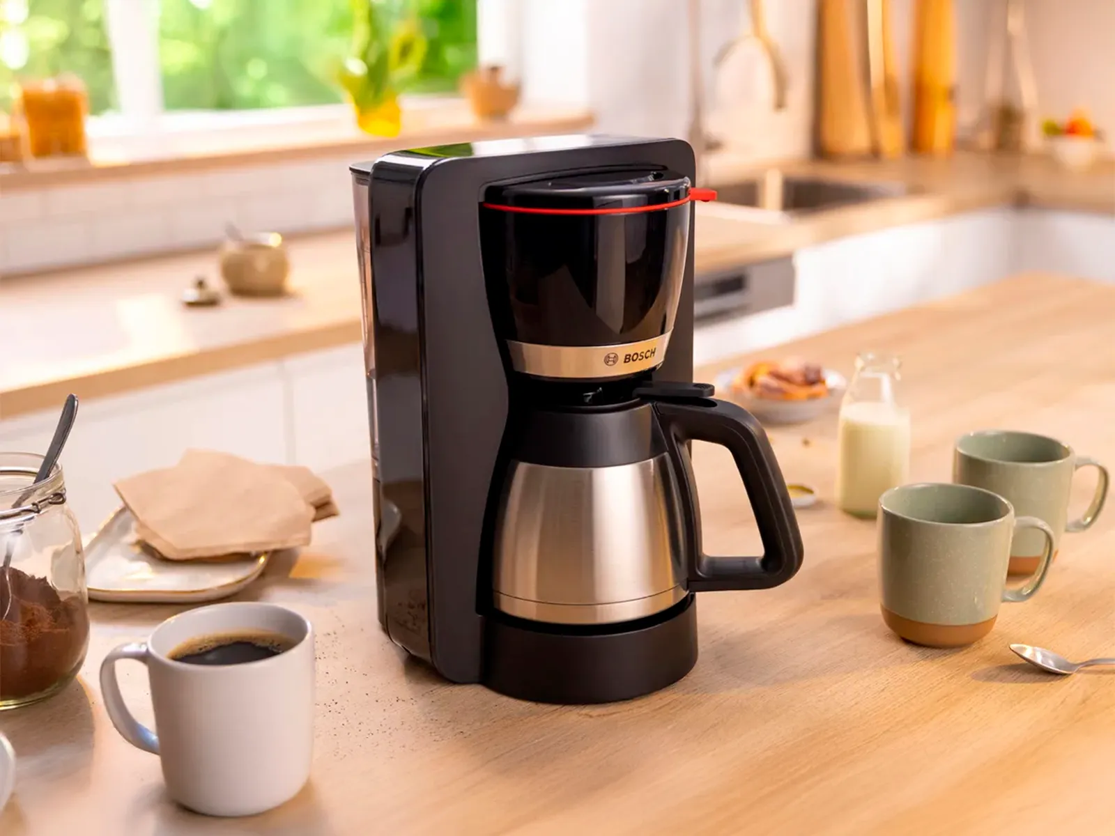 Filter coffee machine with carafe of coffee next to cups on kitchen counter.