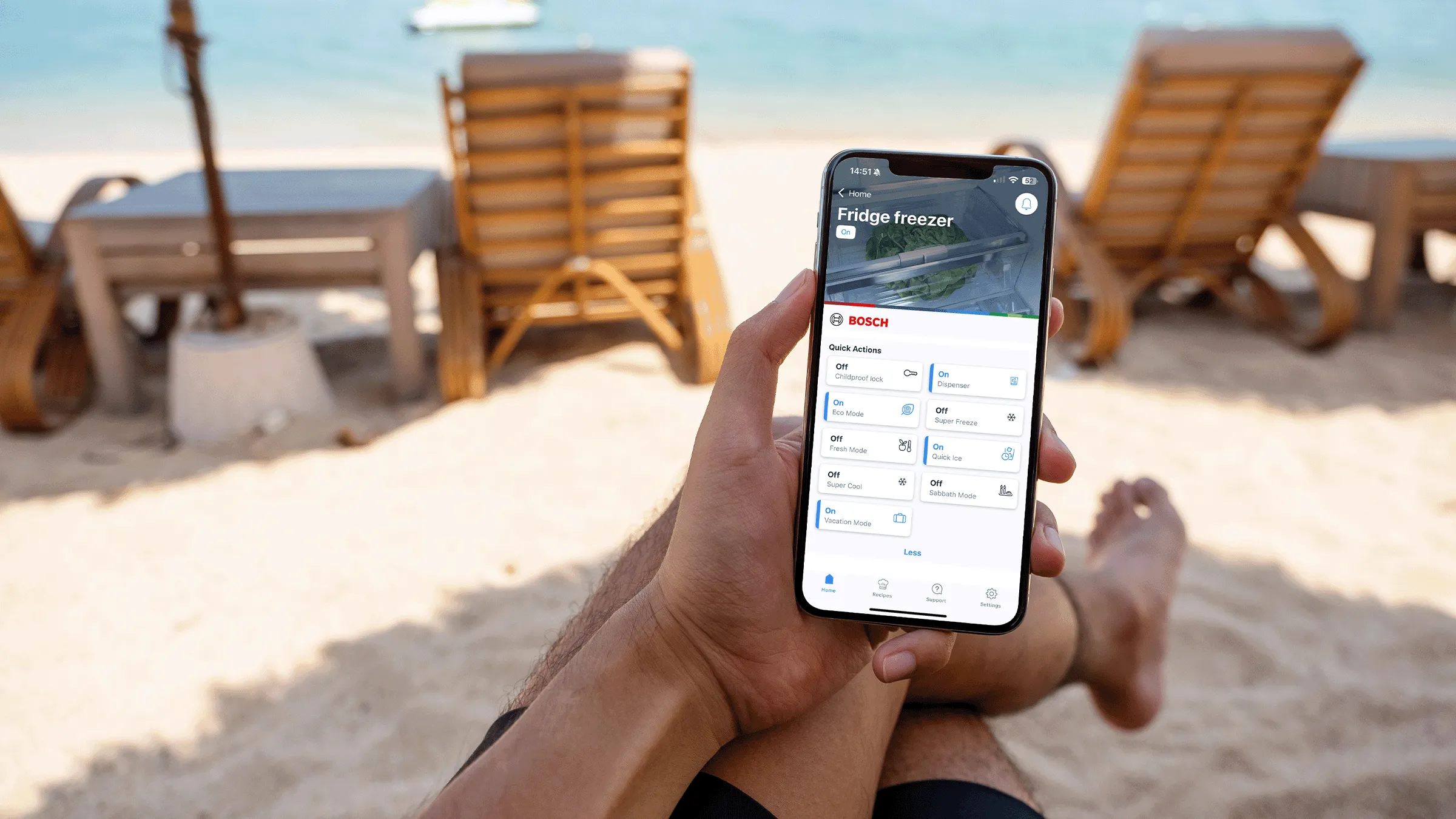 Eine Person am Strand nutzt die Bosch Home Connect App auf dem Smartphone, um Hausgeräte aus der Ferne zu steuern.