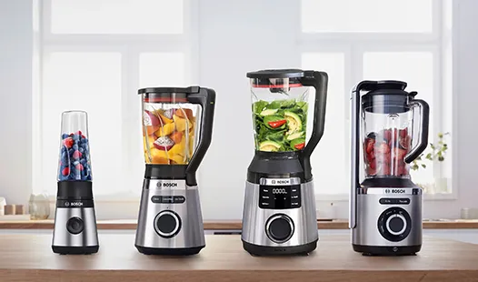 Vier Bosch-Mixer in verschiedenen Größen, mit buntem Obst und Gemüse befüllt, stehen auf einer Küchenarbeitsplatte im natürlichen Licht.