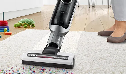 Una persona usa un elegante aspirapolvere su un soffice tappeto bianco, circondata da coriandoli colorati sparsi