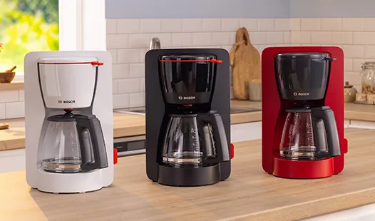 „Drei Bosch-Kaffeemaschinen in Weiß, Schwarz und Rot stehen in einer Reihe auf einer Küchenarbeitsplatte und zeigen modernes Design und Funktionalität.