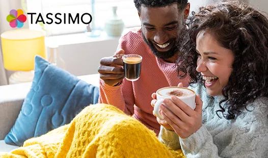 Una pareja disfruta de un café juntos bajo una manta amarilla, rodeados de una sala de estar luminosa y acogedora.