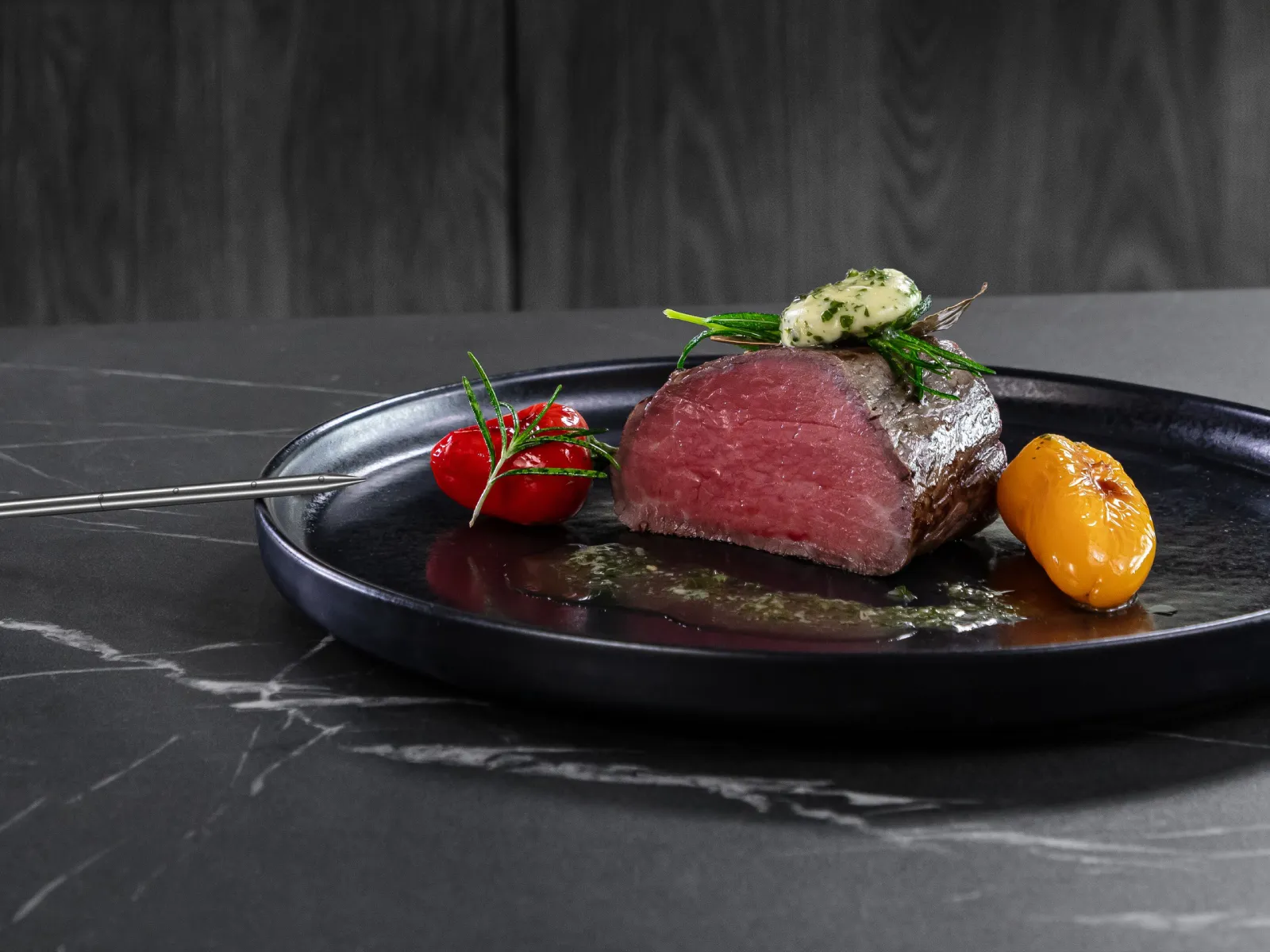 Perfekt gegartes Roastbeef und Ofengemüse auf einem schwarzen Teller, garniert mit Kräutern.