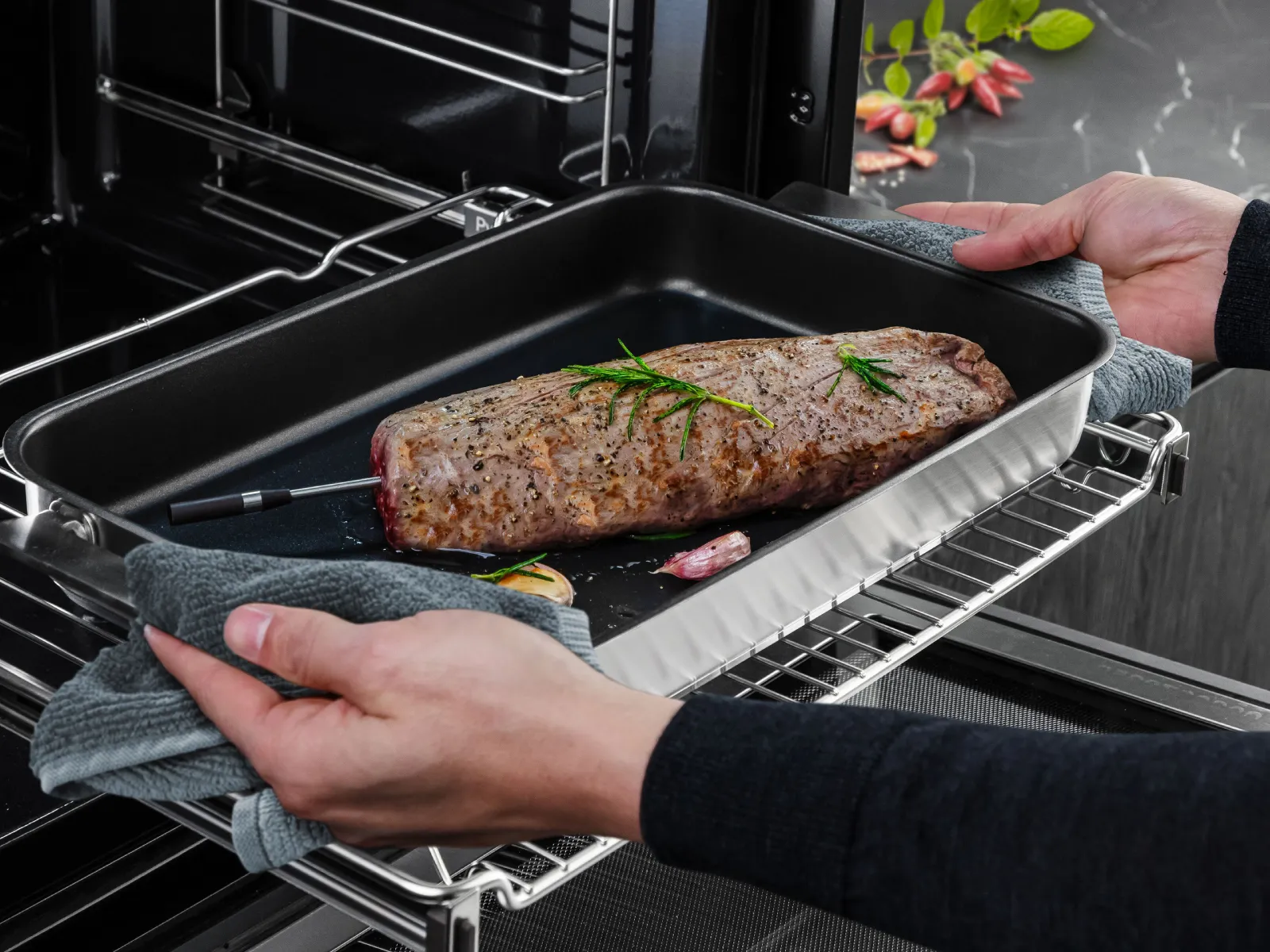 Zwei Hände nehmen ein gegartes Roastbeef mit eingesetztem kabellosen roastingSensor aus dem Ofen.