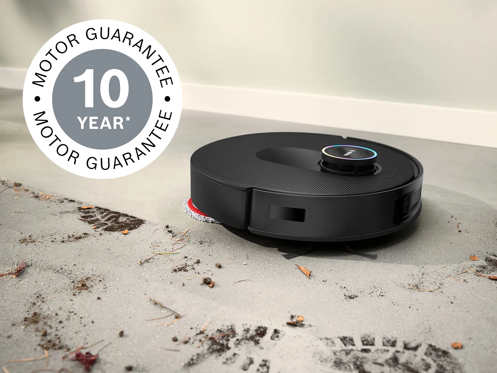 Spotless tīra dubļus no baltām flīzēm, augšējā kreisajā stūrī redzama 10 gadu motora garantijas emblēma.