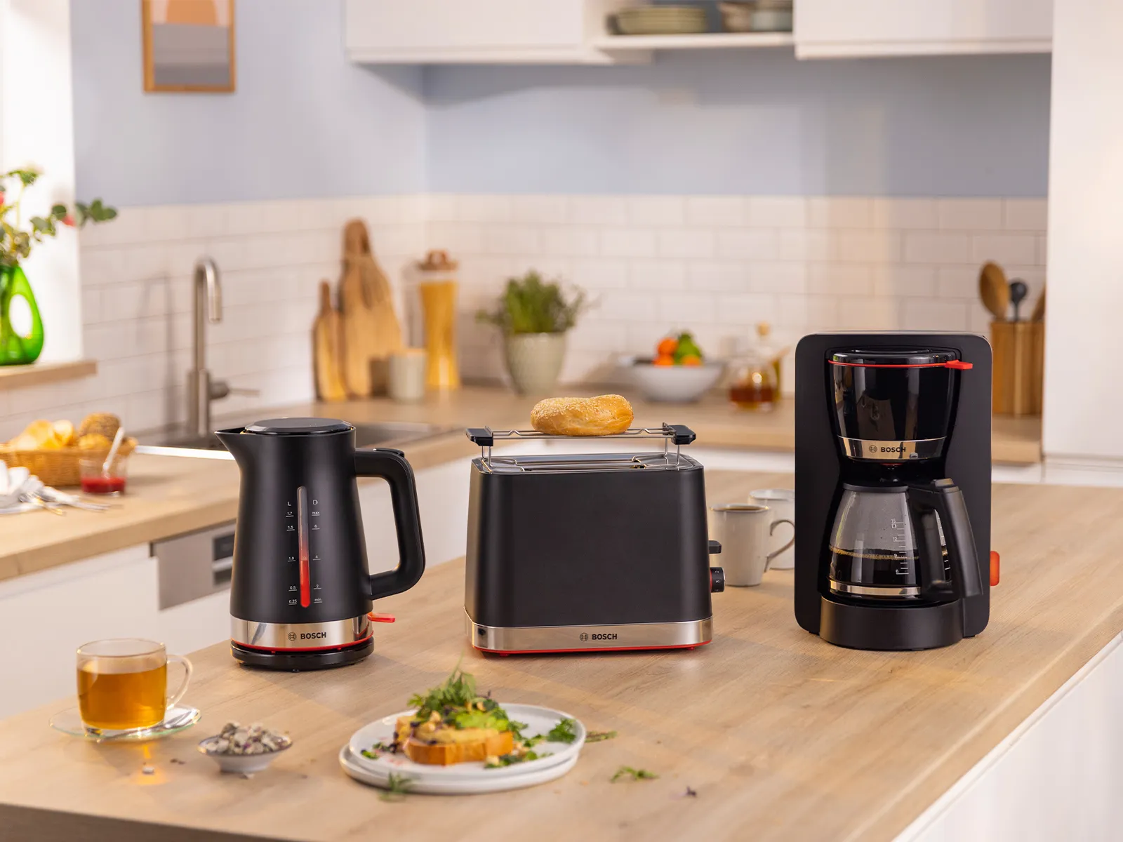 Bosch breakfast set featuring a black kettle, toaster with bread, and coffee maker on a wooden kitchen counter.