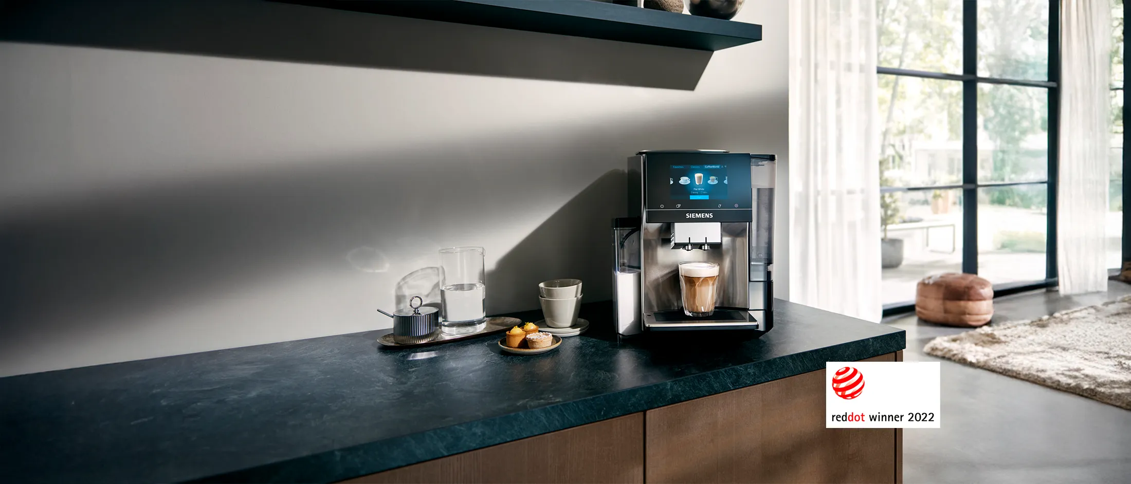 Modern Siemens coffee machine on kitchen counter with a fresh cup of coffee, snacks, and Red Dot Winner 2022 logo.