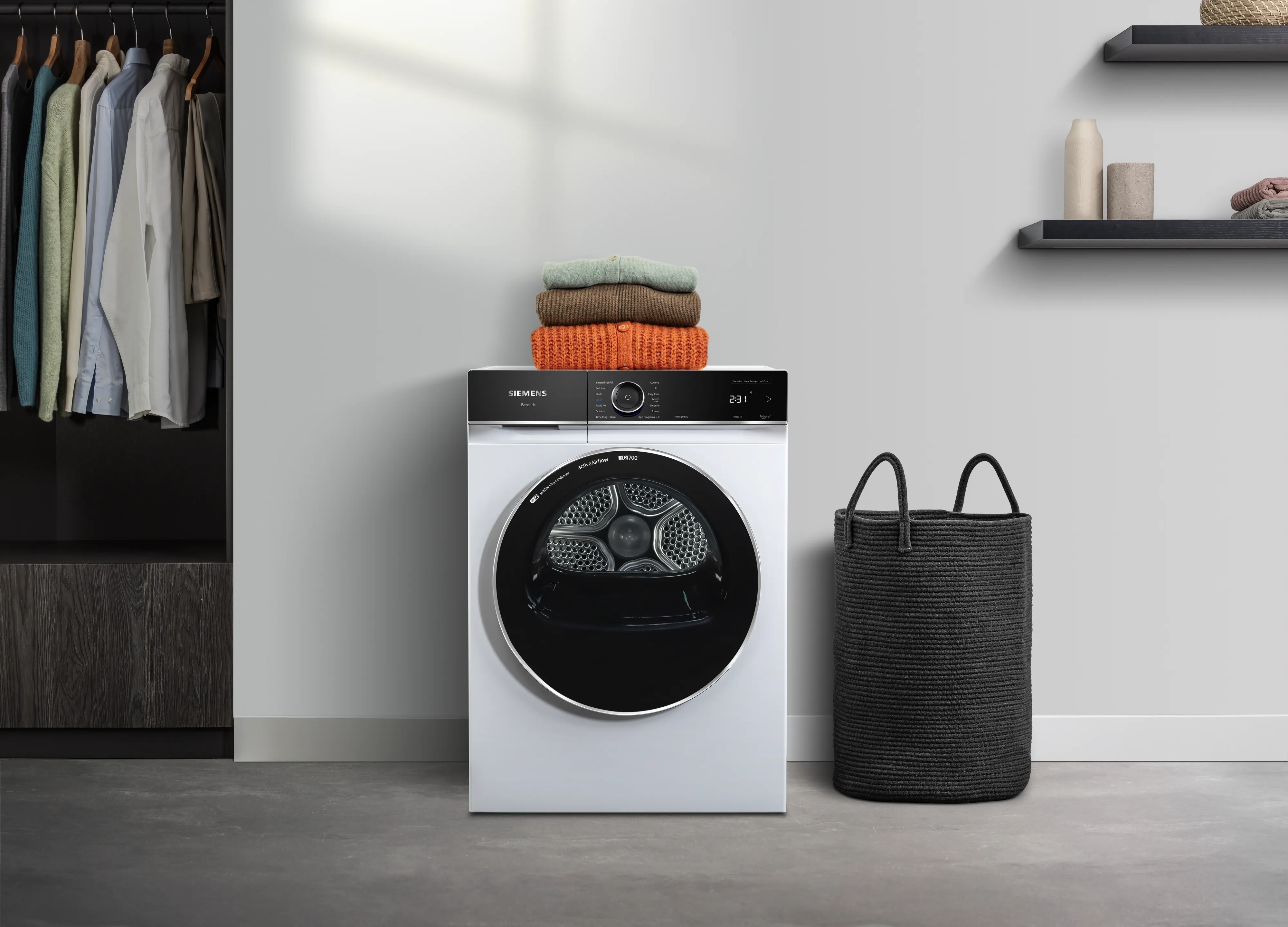 Ein moderner weißer Trockner mit ordentlich gestapelten Handtüchern oben, in einem stilvollen Wäscheraum neben einem schwarzen Wäschekorb und einem Schrank.