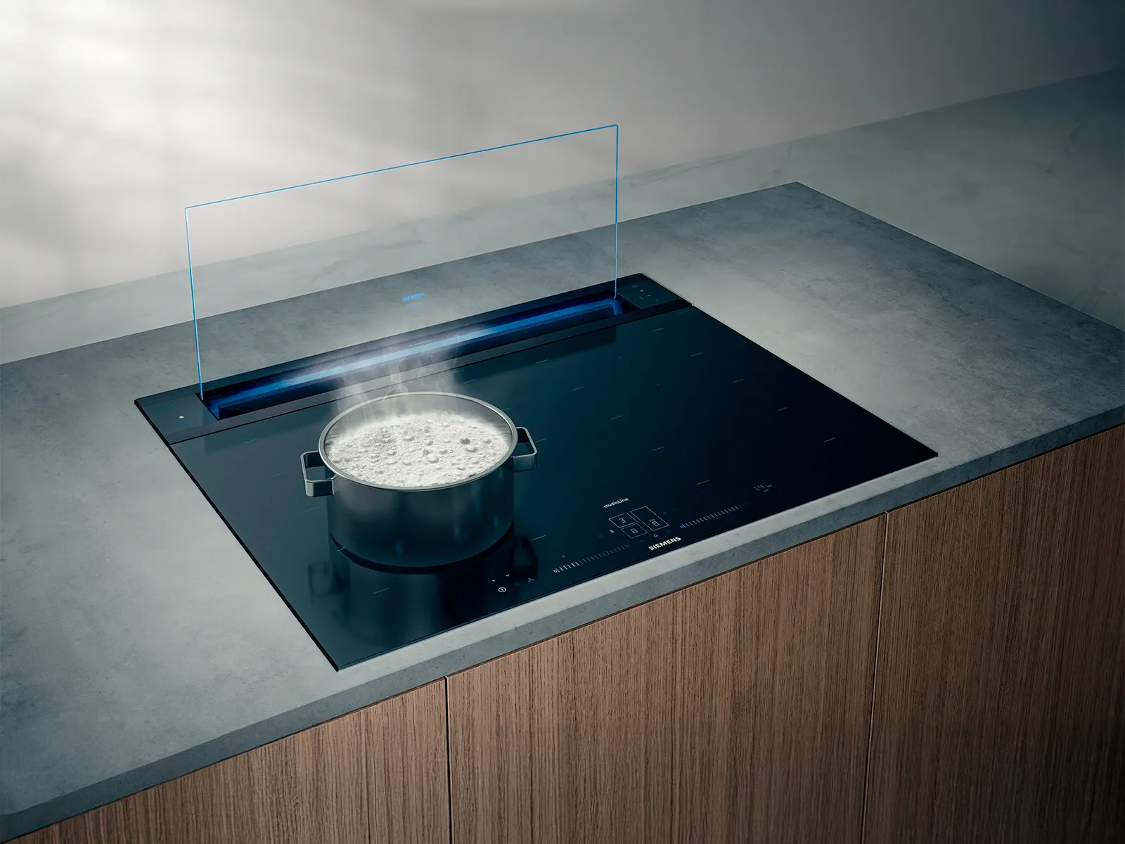 En modern induktionshäll med en gryta med kokande vatten, som har en stilren design och en bänkfläkt integrerad i köksbänken precis ovanför hällen.