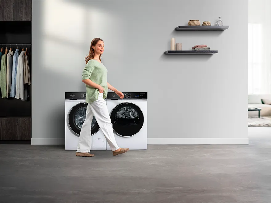 Osoba trzymająca niebieską koszulę przed pralką w nowoczesnej pralni.