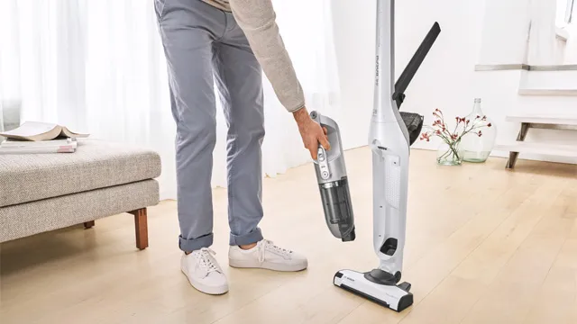 Eine Person in heller Hose reinigt den Boden mit einem weißen Staubsauger und hält eine abnehmbare Handgeräte-Einheit in einer Hand.