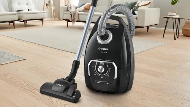 Una aspiradora negra Bosch con una manguera flexible y boquilla para suelos está sobre un suelo de madera clara en una sala de estar moderna.