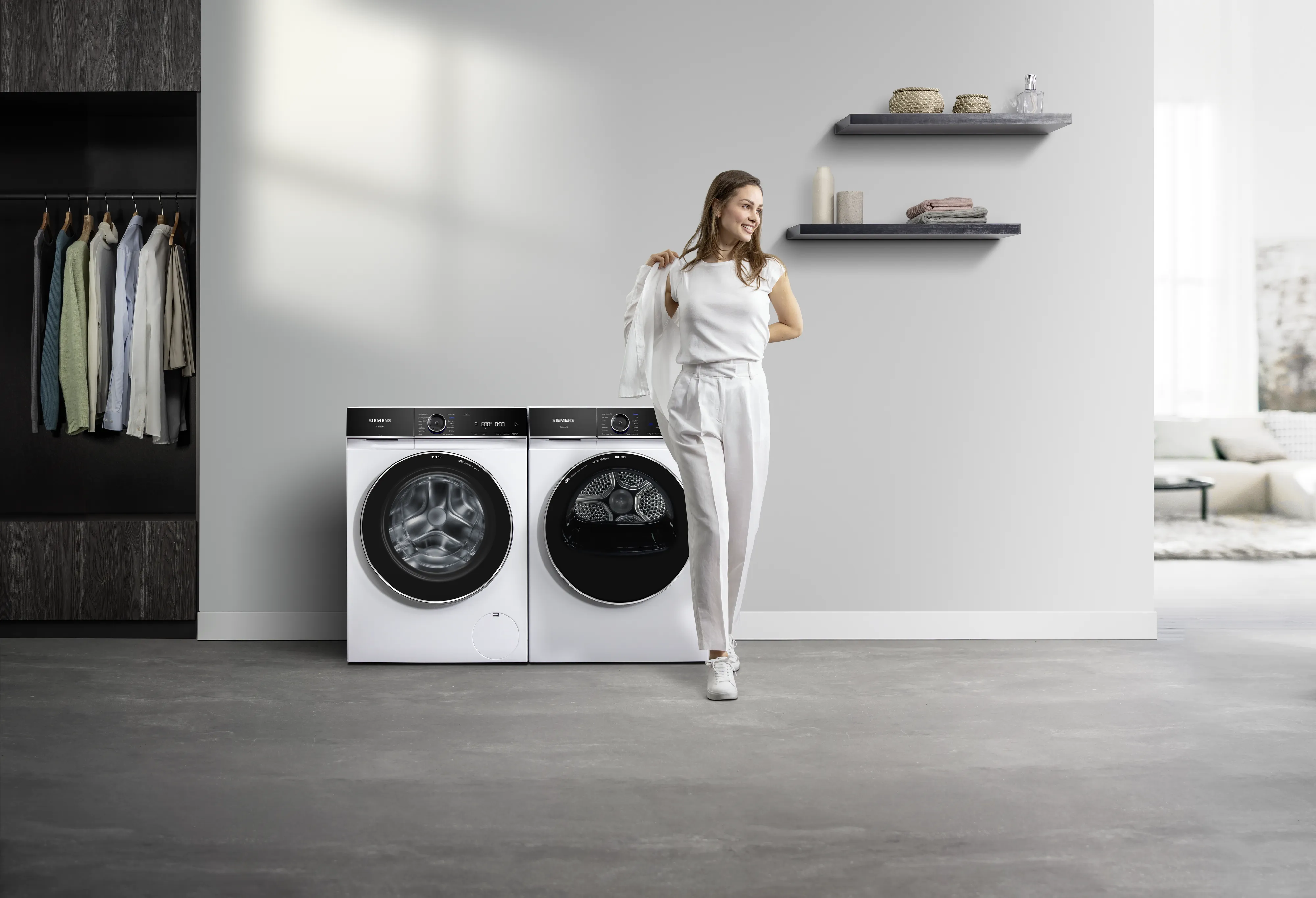 Kobieta w białym eleganckim stroju, stoi przed pralkami 