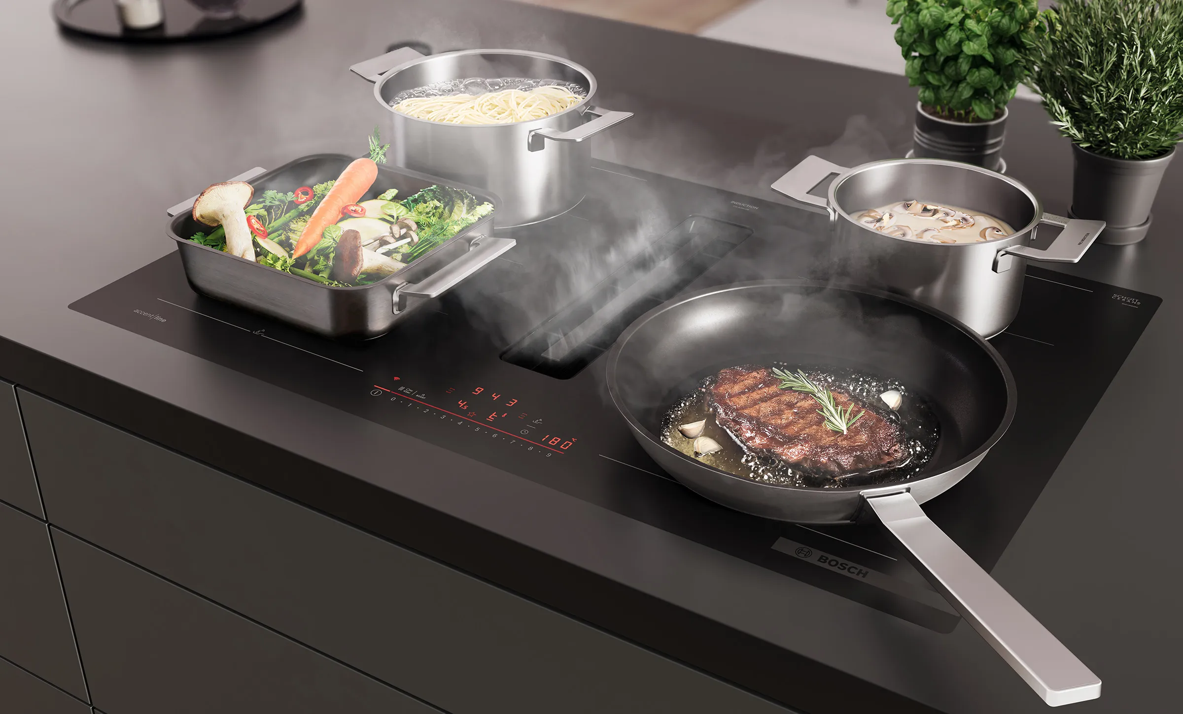 Bosch Kochfeld mit integriertem Dunstabzug. Eine Pfanne mit Steak, zwei Töpfe und eine Auflaufform mit Gemüse auf dem Kochfeld, in der Mitte wird aufsteigender Dampf abgesaugt.