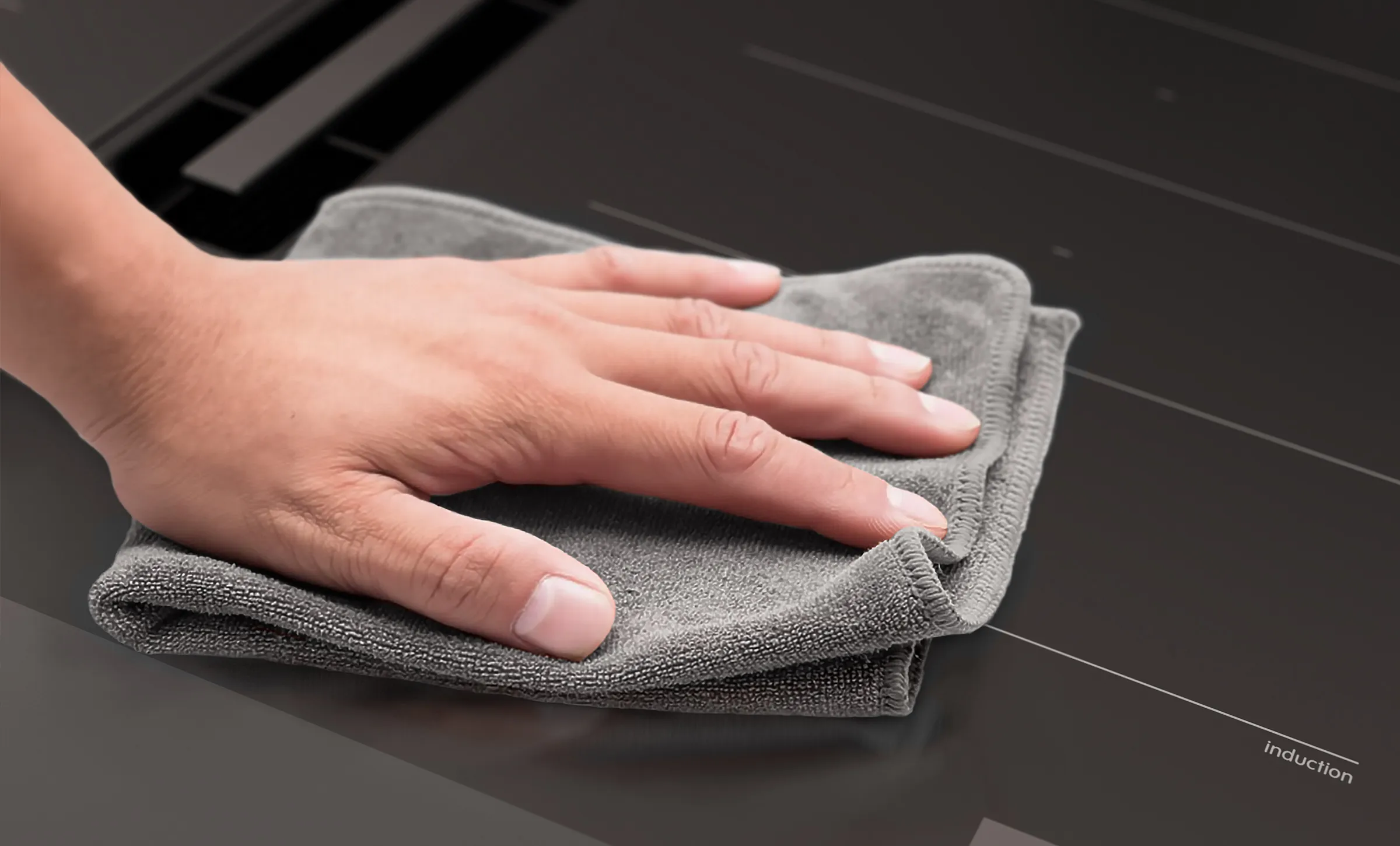 Bosch Induktionskochfeld im Matt Design. Eine Hand wischt mit einem grauen Mikrofasertuch über die mattschwarze Glasoberfläche, unten rechts ist der dezente Schriftzug ‚induction‘ zu sehen.
