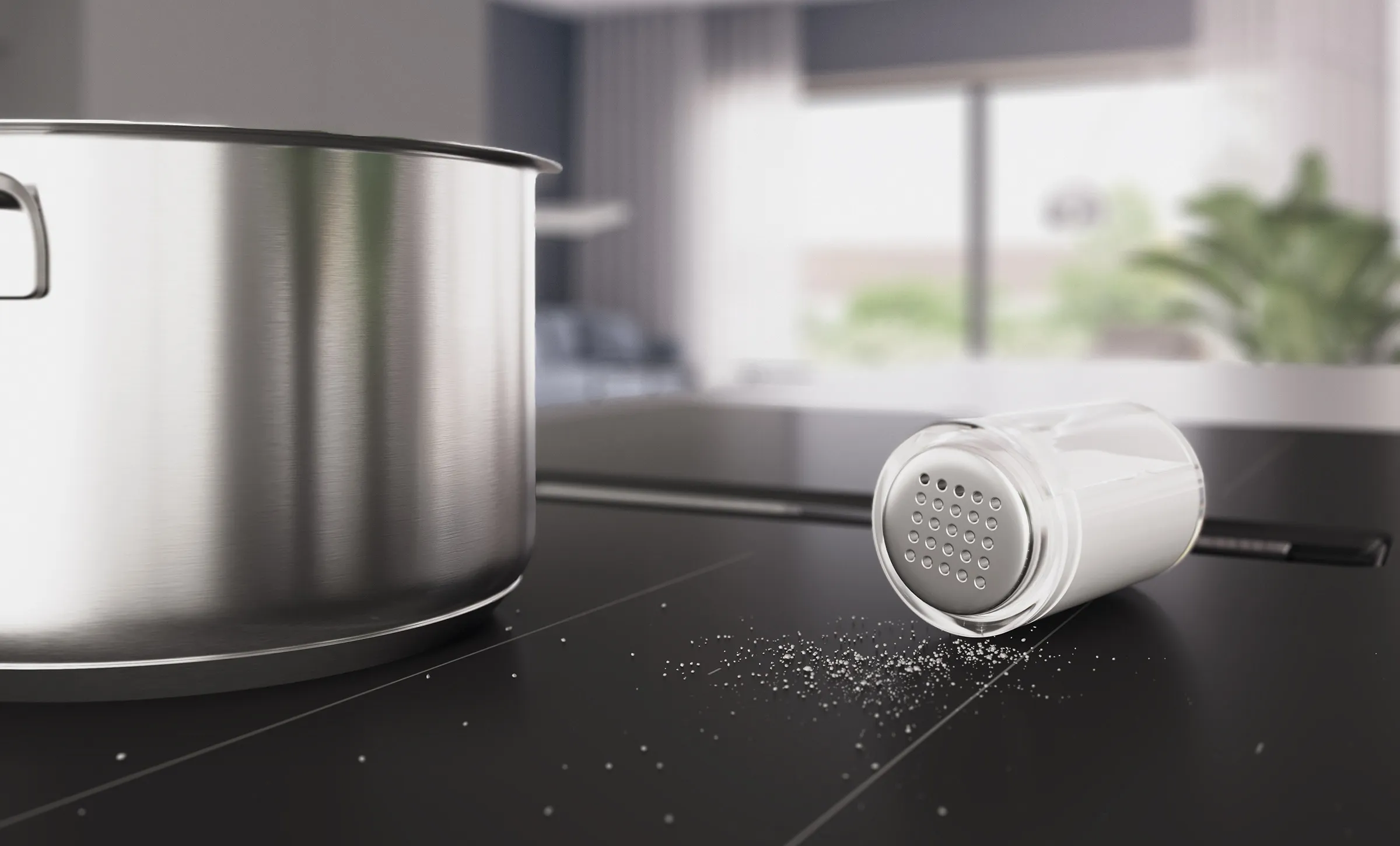 Bosch Kochfeld im Matt Design. Ein großer Kochtopf aus Edelstahl und ein umgekippter Salzstreuer mit verstreuten Salzkörnern auf der mattschwarzen Oberfläche, im Hintergrund ein heller, verschwommener Wohnbereich.