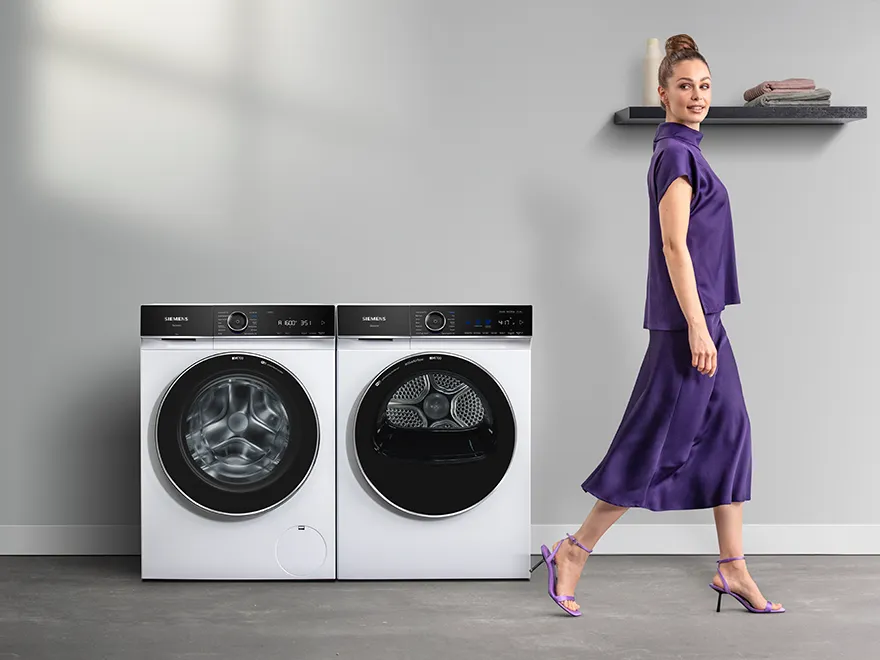 Una mujer elegantemente vestida pasa frente a un conjunto de lavadora y secadora Siemens