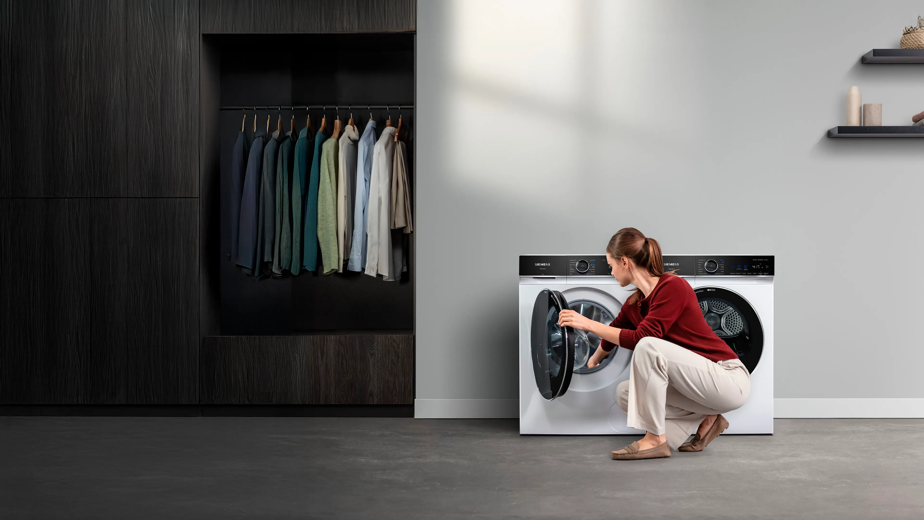 Eine Siemens iQ700 Waschmaschine steht neben einem iQ700 Trockner. Eine Frau legt Wäsche in die Wäschetrommel