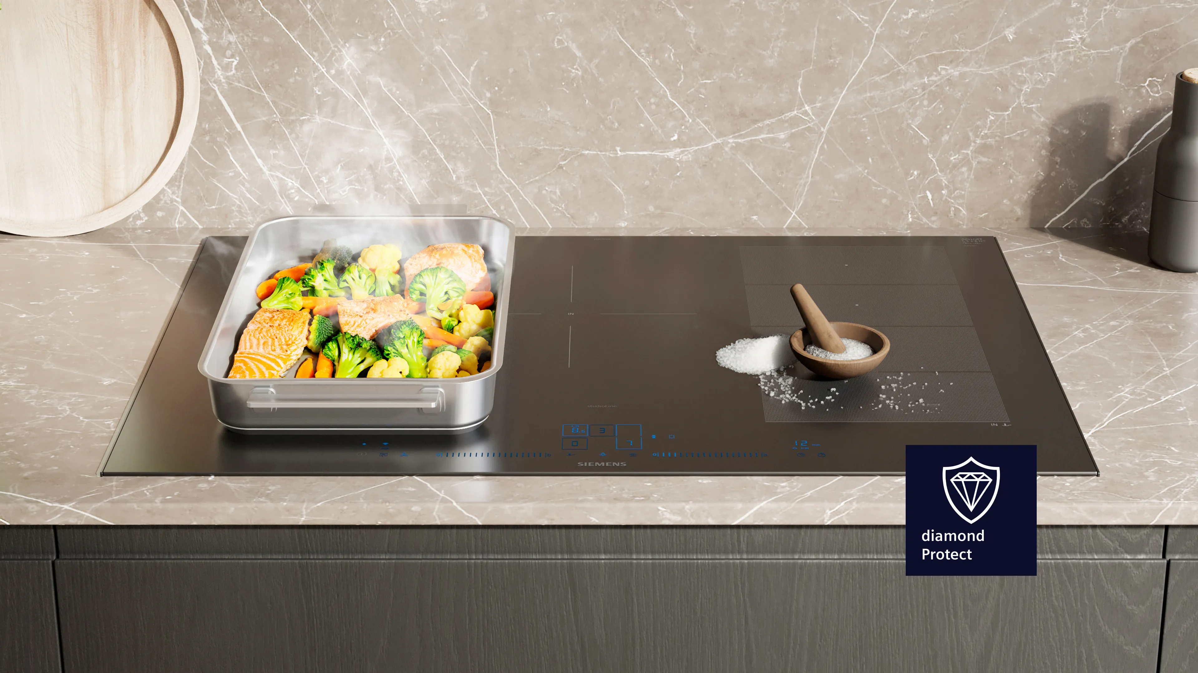 Plaque à induction moderne sur laquelle cuisent à la vapeur du saumon et des légumes dans une poêle, avec du sel dans un bol en bois posé sur un plan de travail en marbre.