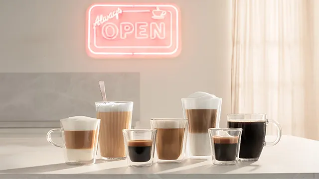 Eine Reihe verschiedener Kaffeegetränke in Glastassen, mit einem Neonzeichen ‚Always Open‘ im Hintergrund und Sonnenlicht, das durch Vorhänge strömt.
