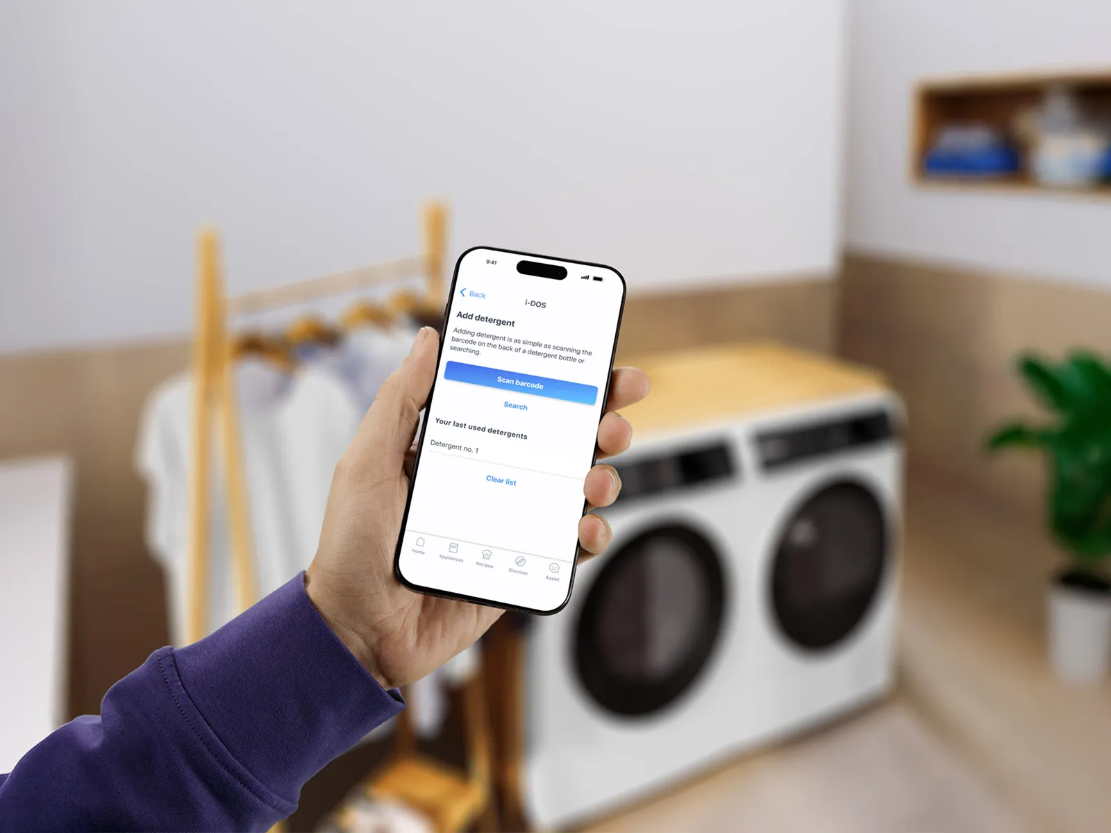 Eine Person hält ein Smartphone, das eine App zum Hinzufügen von Waschmittel anzeigt.