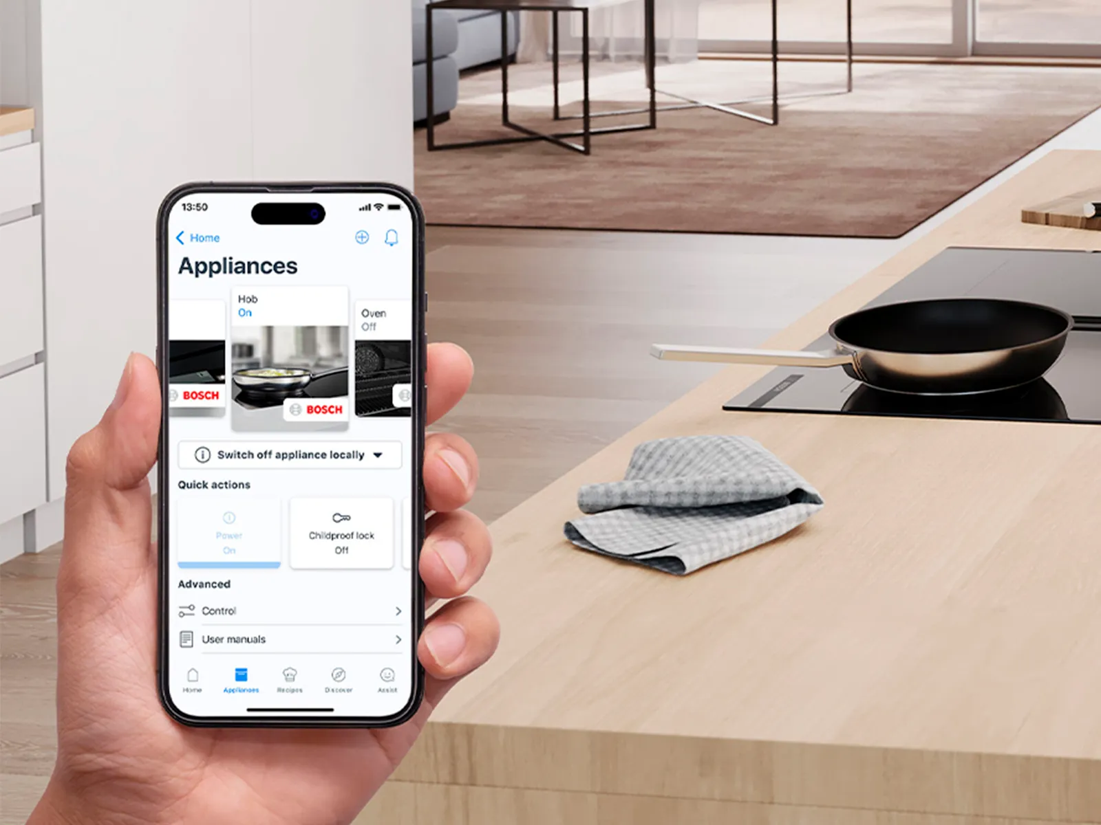 A person holds a smartphone displaying a smart appliance control app, set in a modern kitchen.