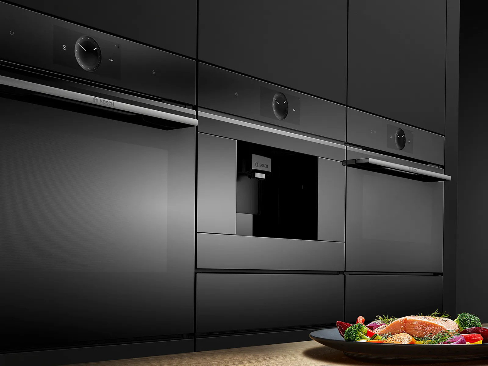 A modern kitchen with black cabinetry featuring built-in appliances and a plate of salmon with vegetables.