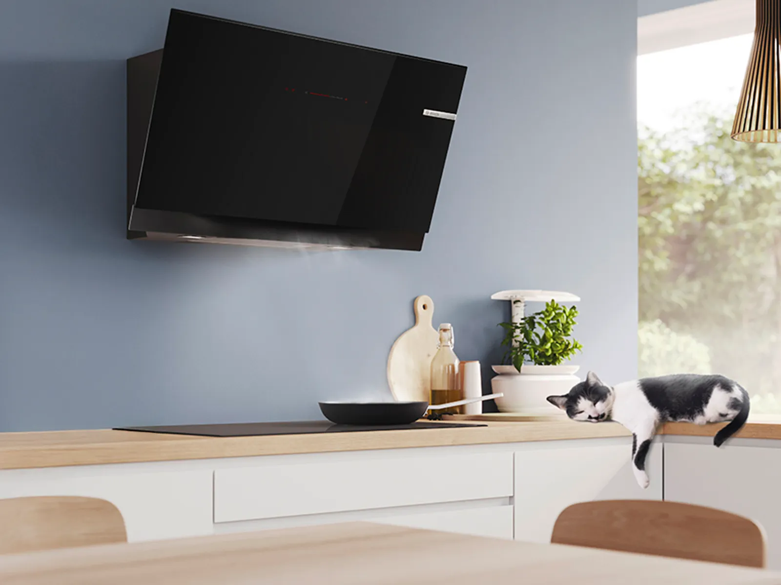 A sleek black kitchen hood hovers above a steaming pot, while a cat lounges on the countertop.