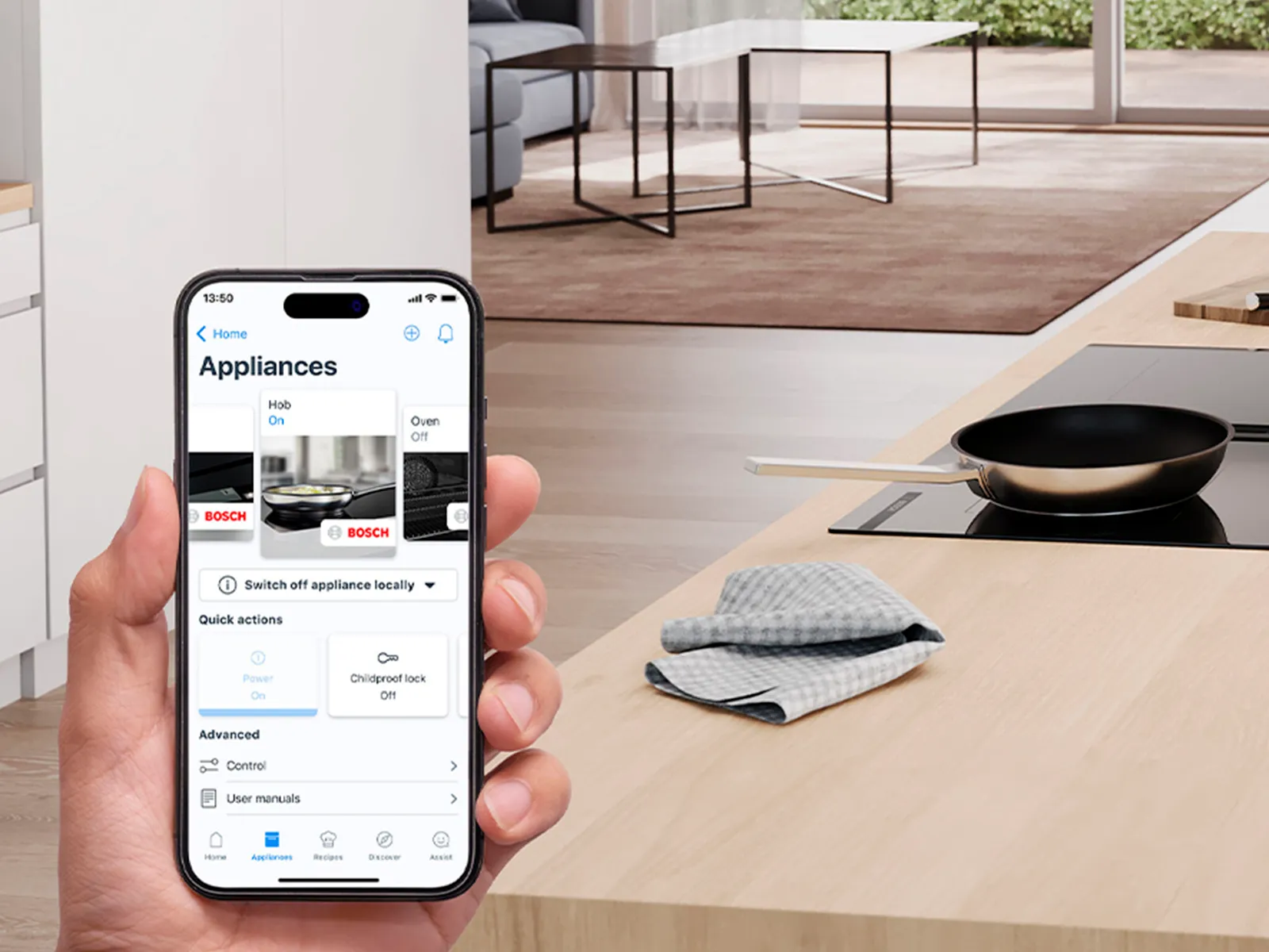 A person holds a smartphone displaying a smart appliance app in a modern kitchen.