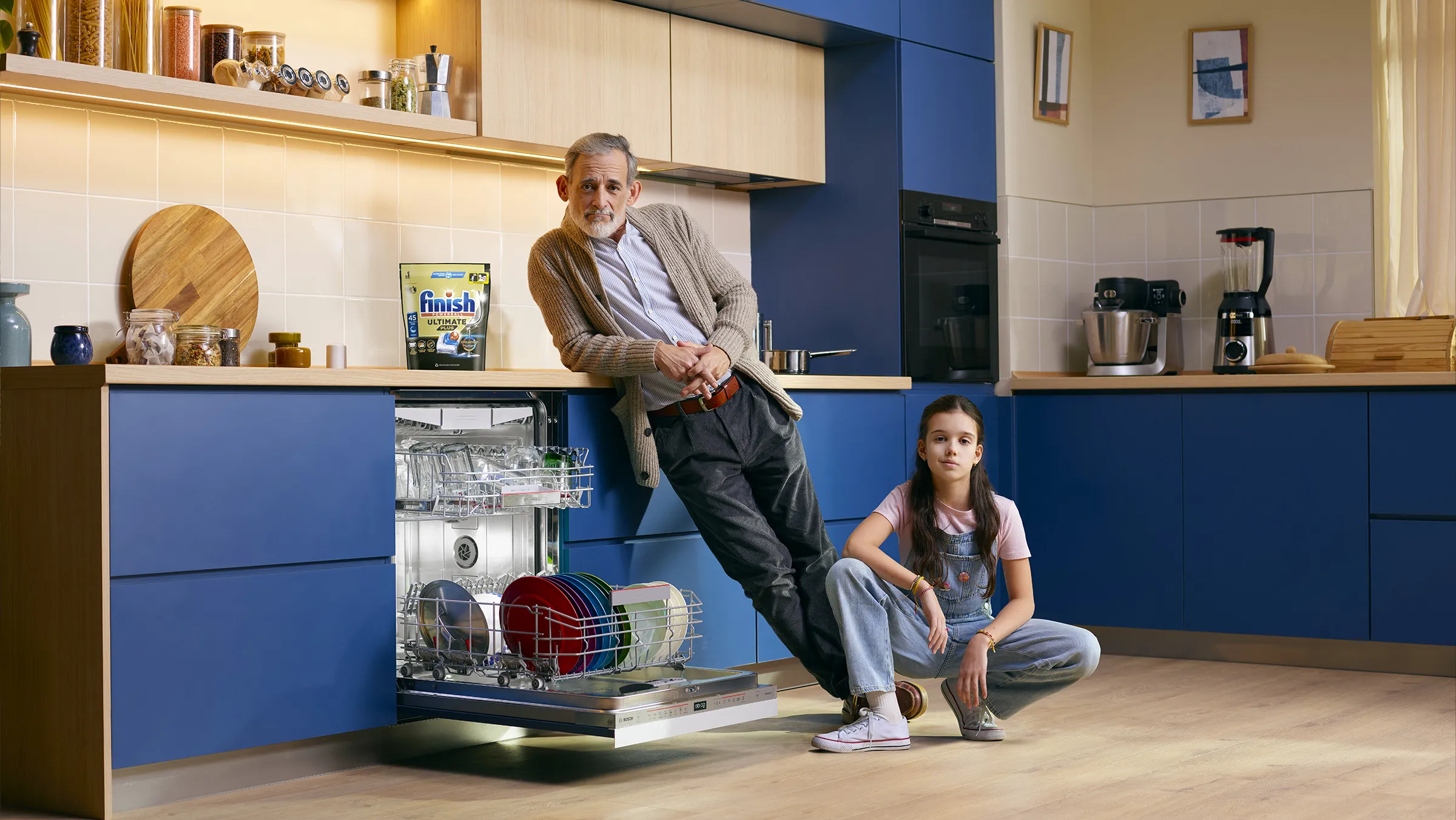 Man leaning against an open dishwasher and girl sitting on the floor in a modern kitchen