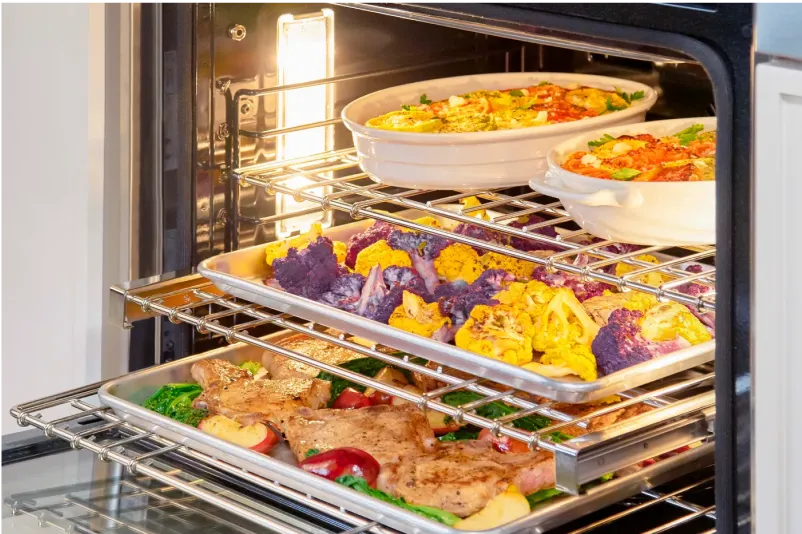 An oven filled with roasted vegetables, chicken, and casseroles, showcasing colorful dishes on multiple racks.