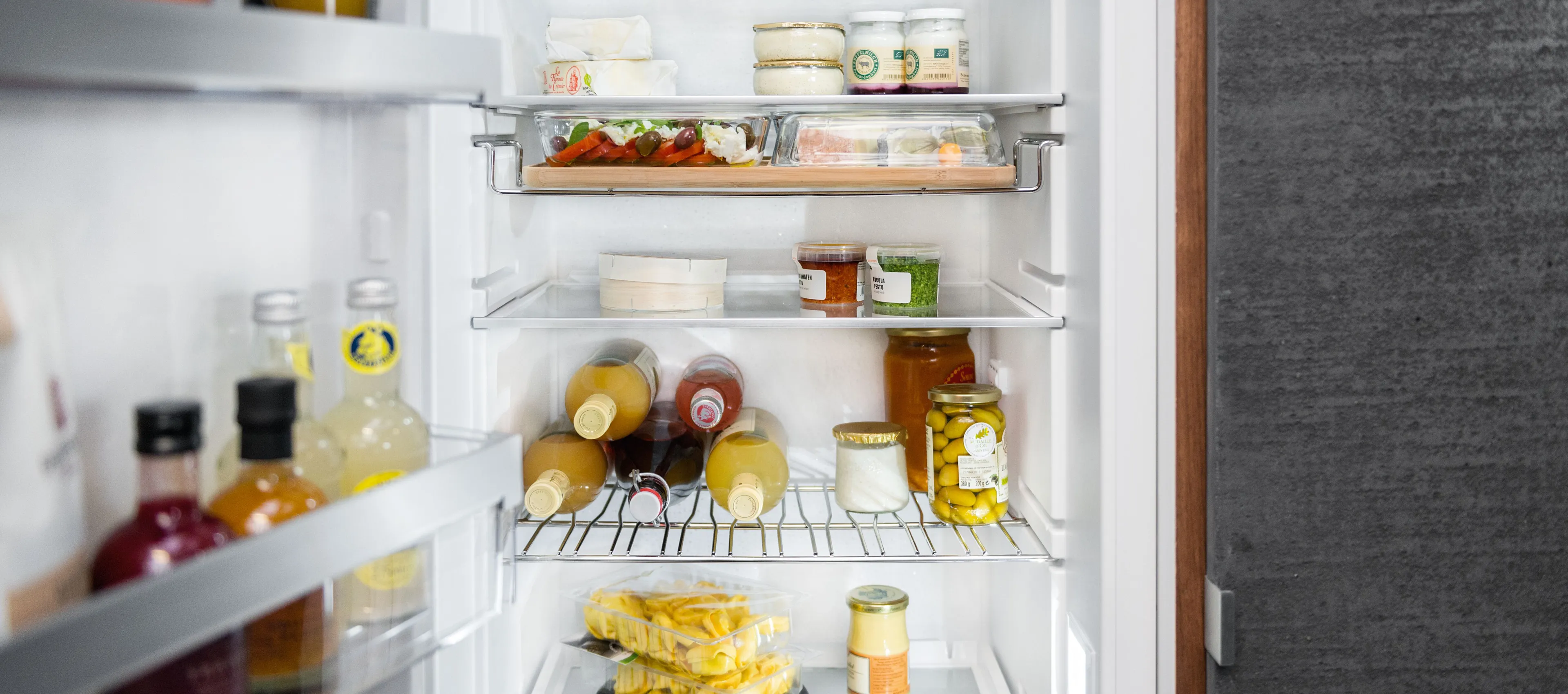 Innenraum eines NEFF Kühlschranks mit mehreren Glasablagen, Gourmet Tray, Flaschenlagerung auf dem Bottle Flex Shelf und einer Auswahl an frischen Lebensmitteln wie Fleisch, Obst und Getränken.