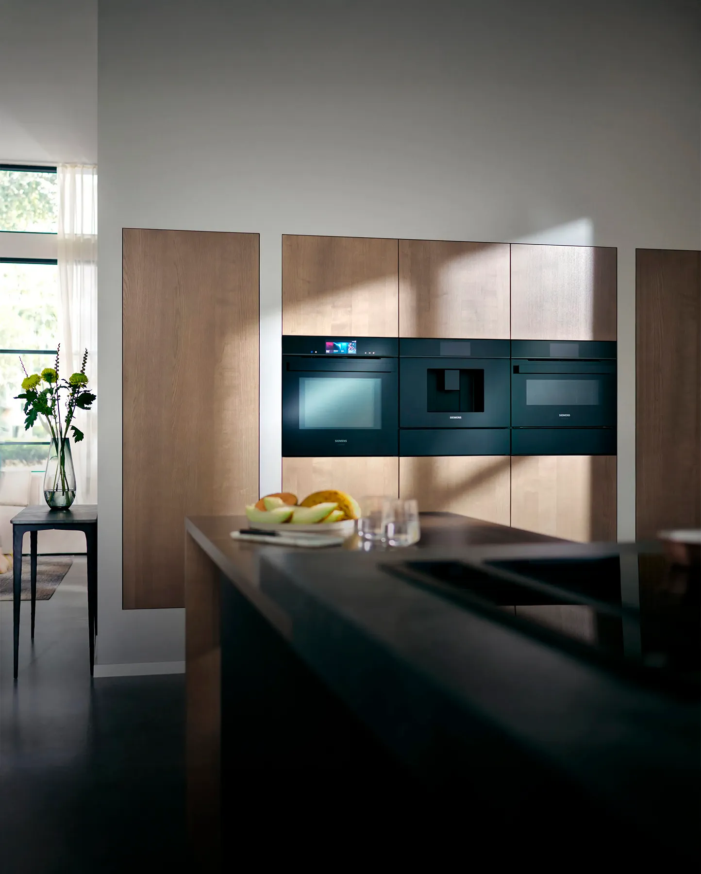 A person holds a smartphone displaying a modern Siemens kitchen with sleek appliances against a light wood backdrop.