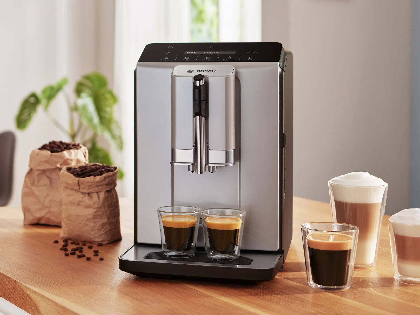 Koffiezetapparaat met espresso bekers op houten tafel, papieren zak met koffiebonen, en potplant op de achtergrond.