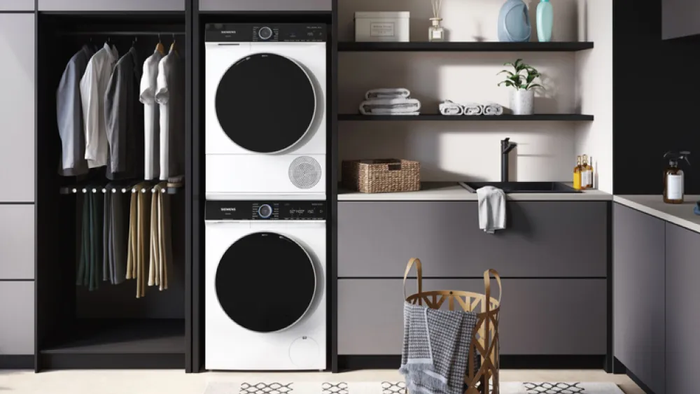 Siemens tvättmaskin och torktumlare är staplade ovanpå varandra i ett inbyggt skåp som är i ett modernt grått tvättrum.