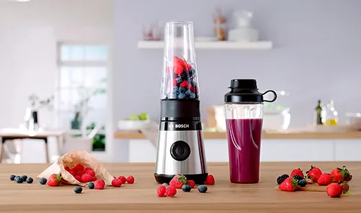 Um liquidificador Bosch com frutos vermelhos no interior está sobre uma mesa de madeira.