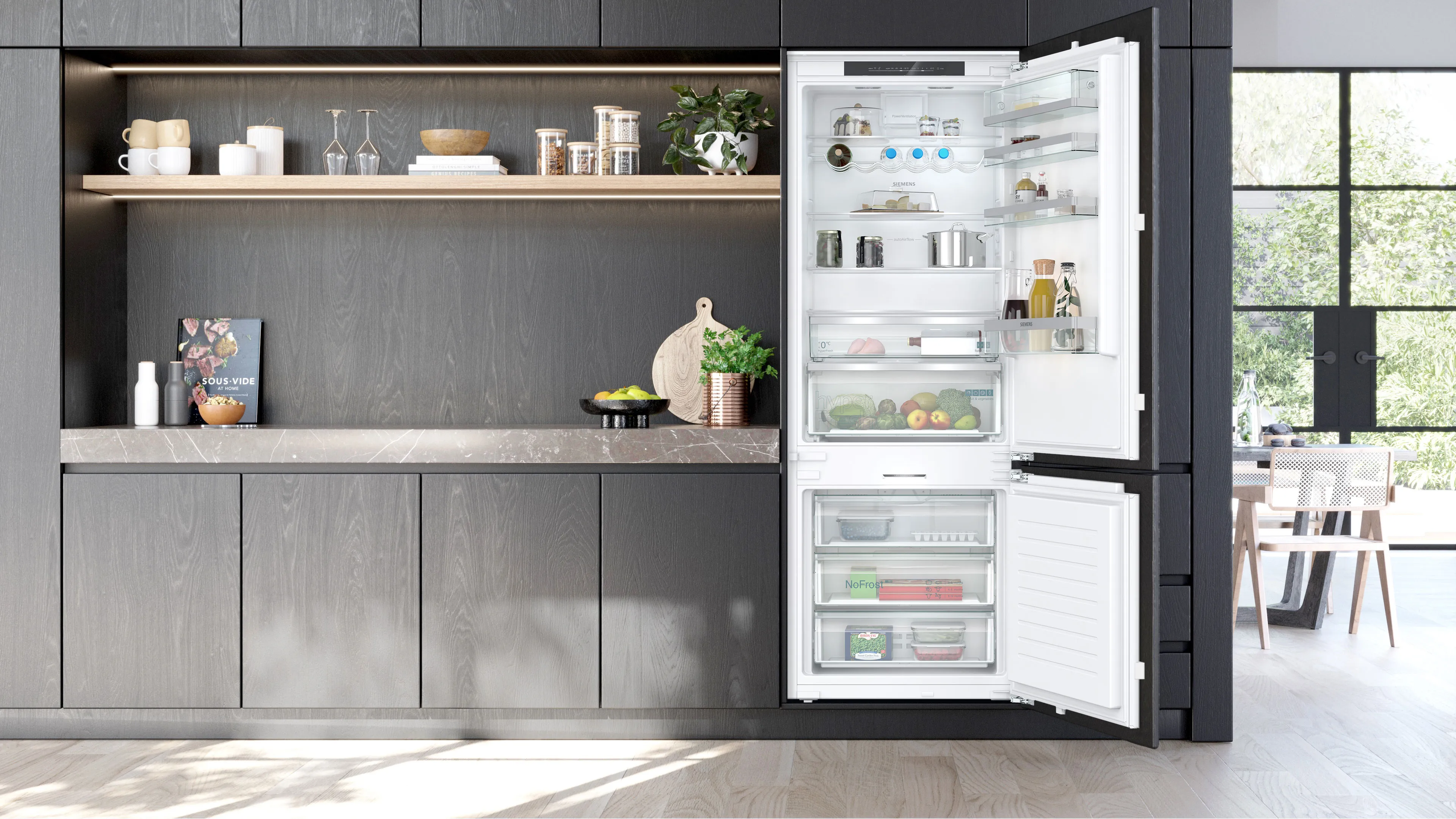 Cucina moderna con mobili grigi, frigorifero aperto con ripiani pieni di alimenti e grande finestra che illumina la stanza