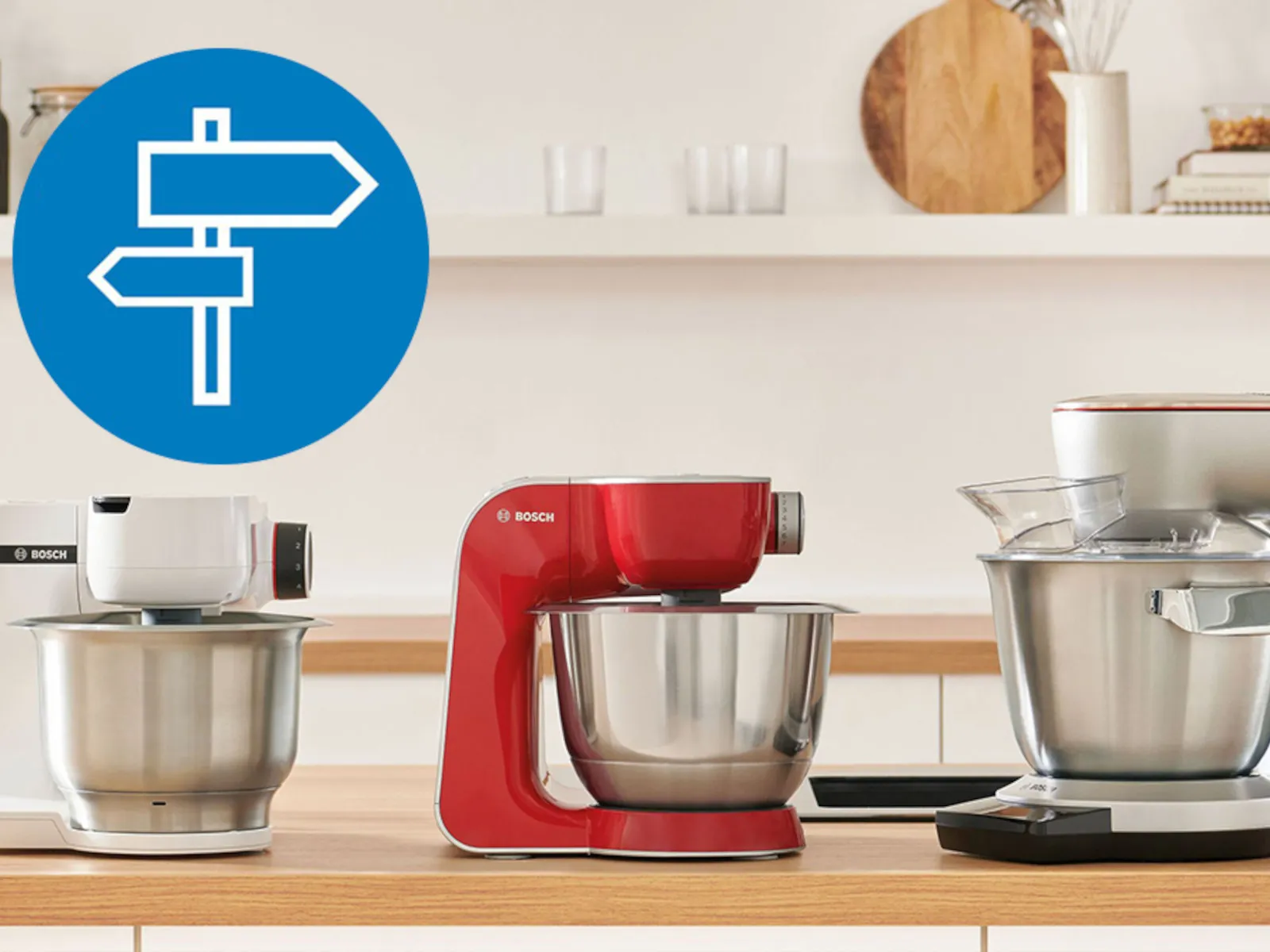 Blat kuchenny z trzema mikserami Bosch w kolorach białym, czerwonym i srebrnym oraz ikoną drogowskazu. 