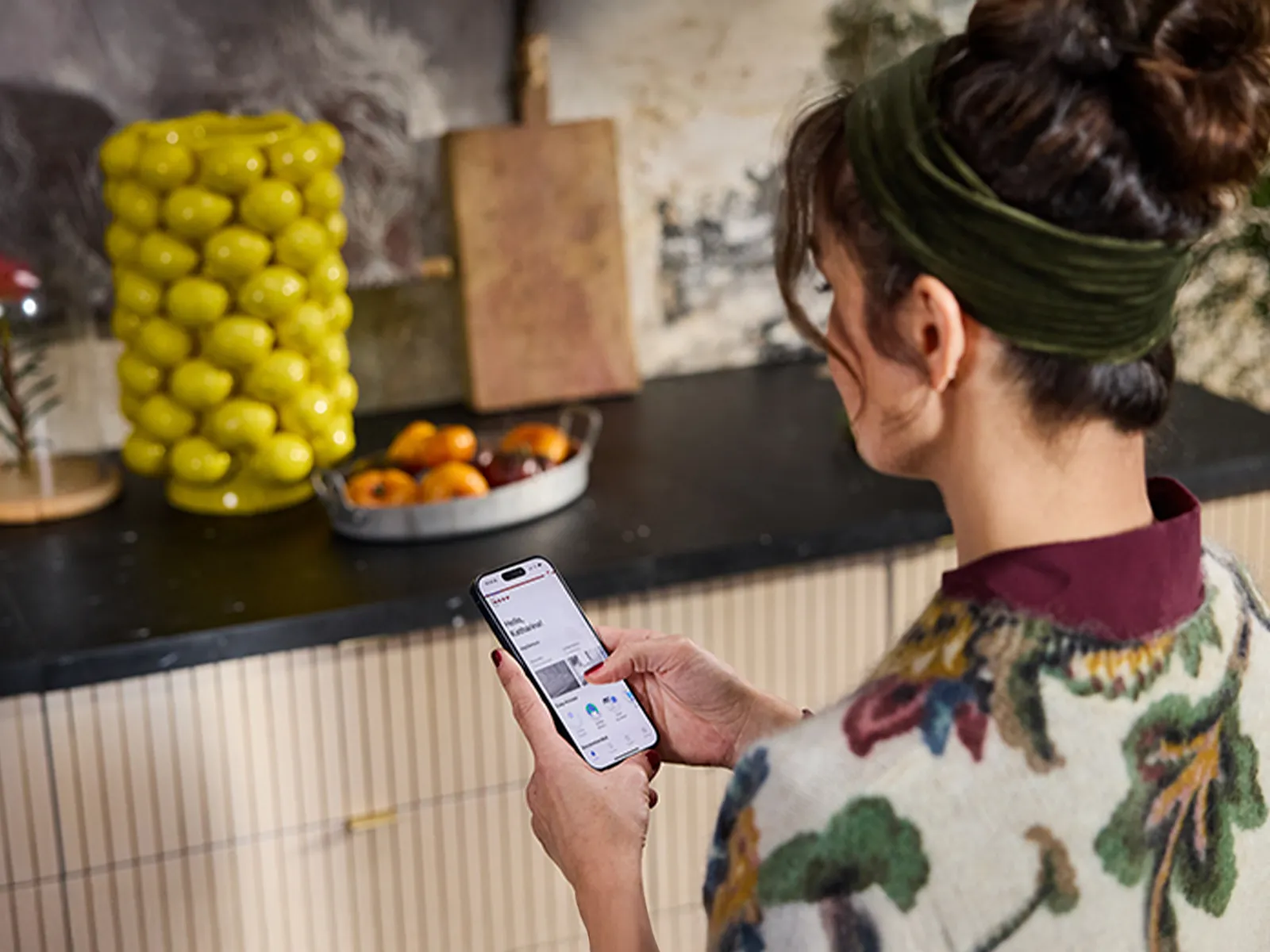 Femme utilisant un smartphone dans une cuisine avec un plan de travail sur lequel se trouvent des citrons et des oranges.