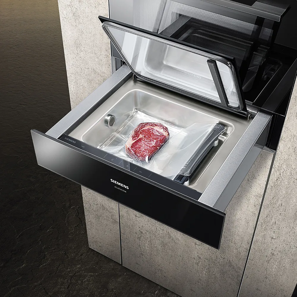 A modern Siemens vacuum sealer drawer with an open lid, containing a packaged steak inside a stainless steel compartment.