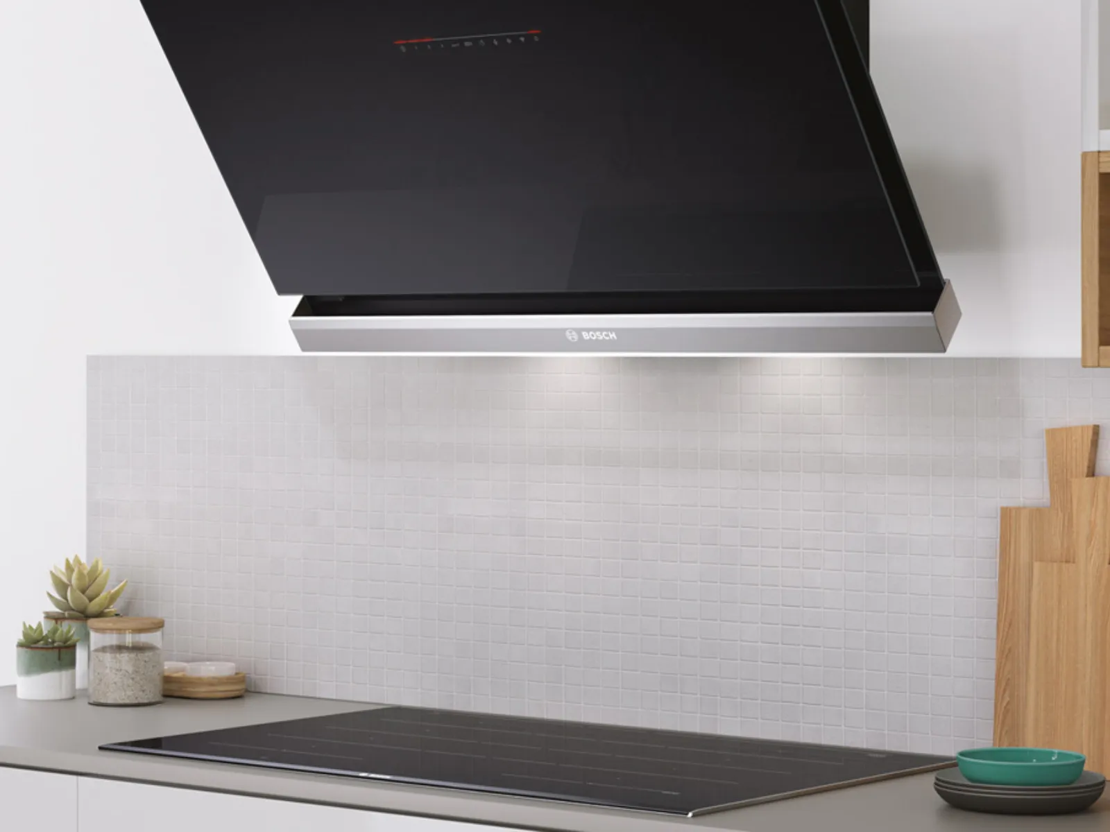 Eine moderne Bosch-Dunstabzugshaube über einer eleganten schwarzen Kochplatte, ausgestattet mit einer strukturierten weißen Rückwand und minimalistischen Holz-Küchenaccessoires.