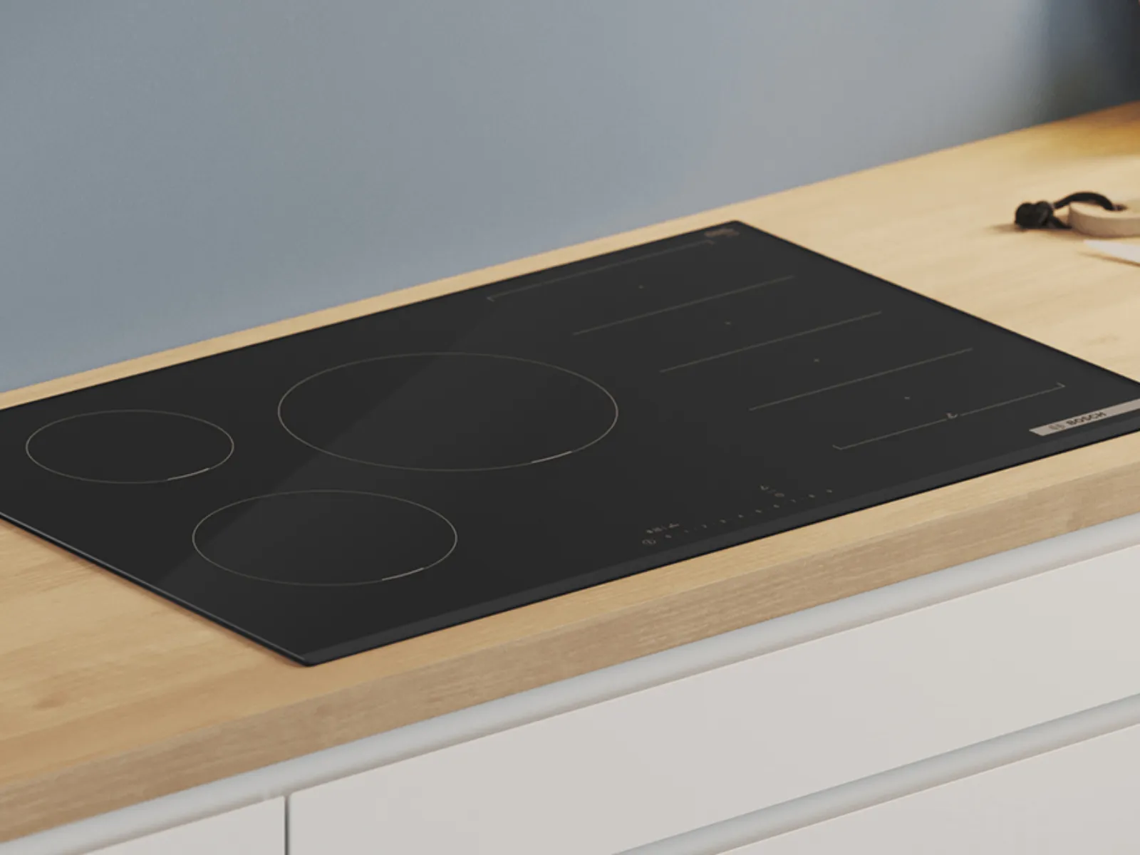 Induktionskochfeld mit drei runden Kochzonen auf einer Küchenarbeitsplatte aus Holz.