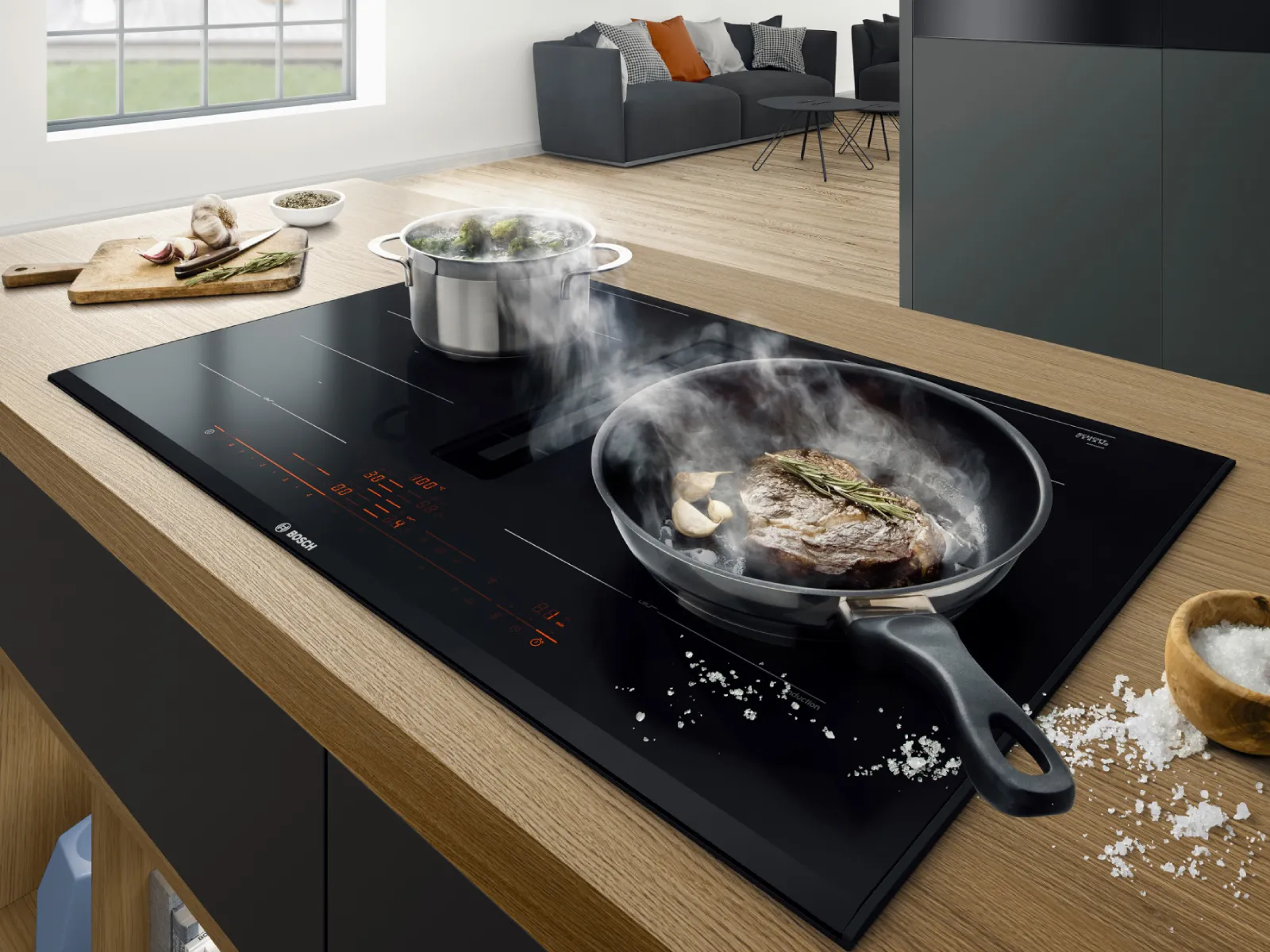 Moderne Küche mit Induktionskochfeld, Kochutensilien und im Hintergrund ein gemütlicher Wohnbereich.