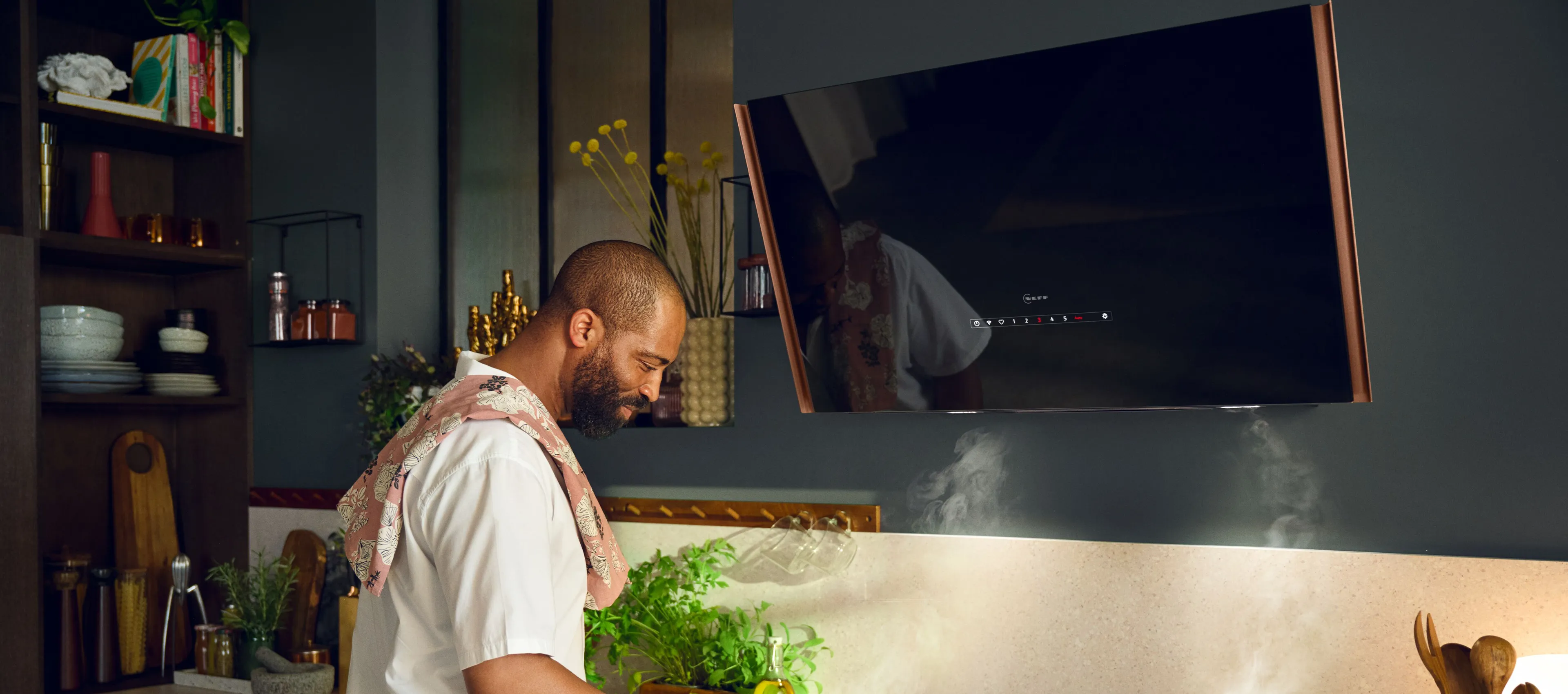 A man prepares food on a stove in a kitchen featuring an angled cooker hood.